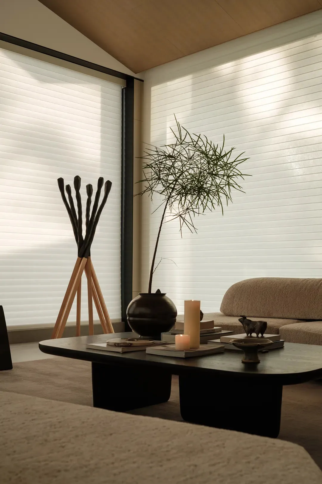 A minimalist living space featuring textured cotton blinds, a coffee table, and a potted plant.