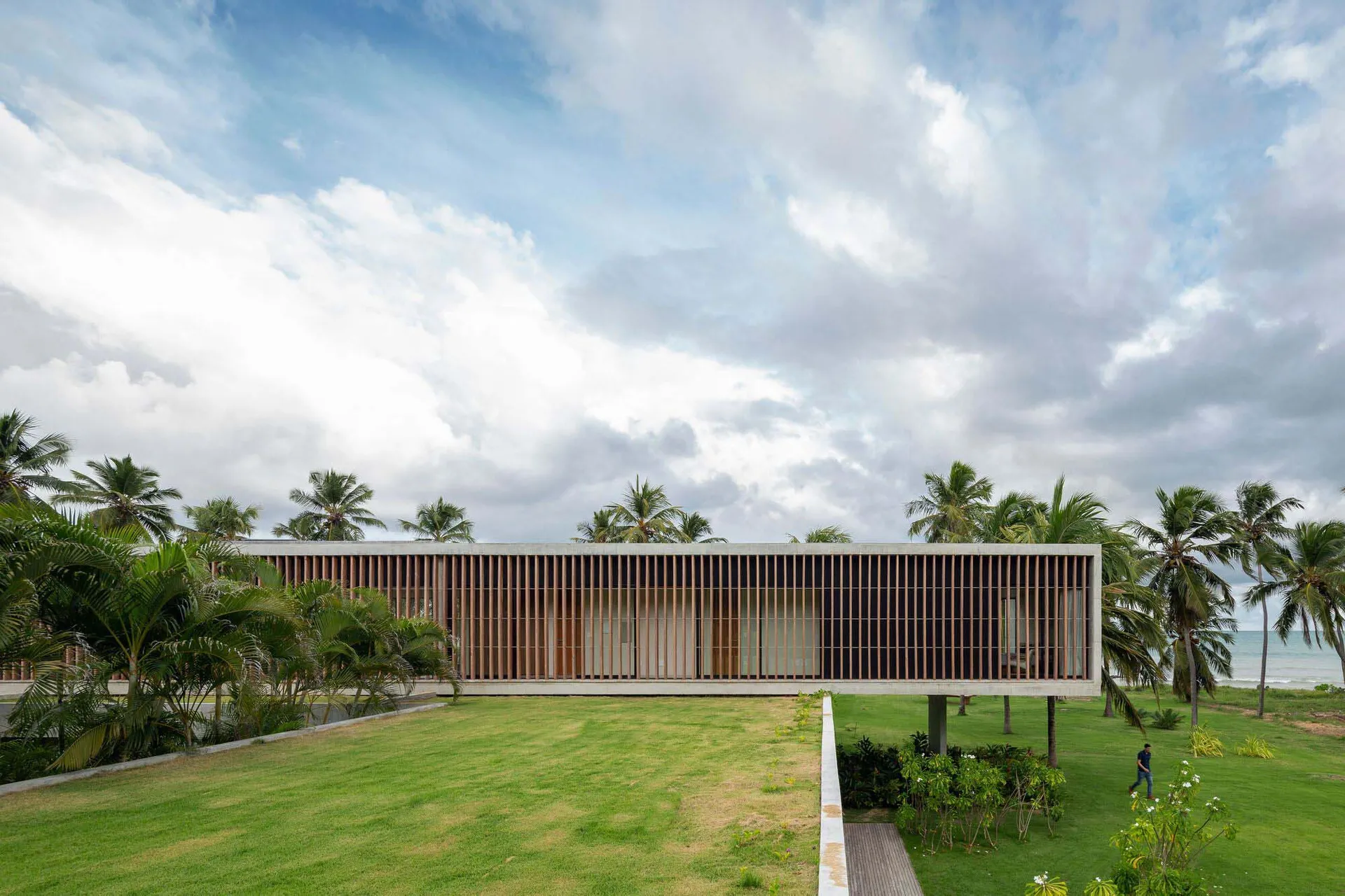 Modern architectural exterior with wooden and concrete materials, set against a cloudy sky and surrounded by greenery.