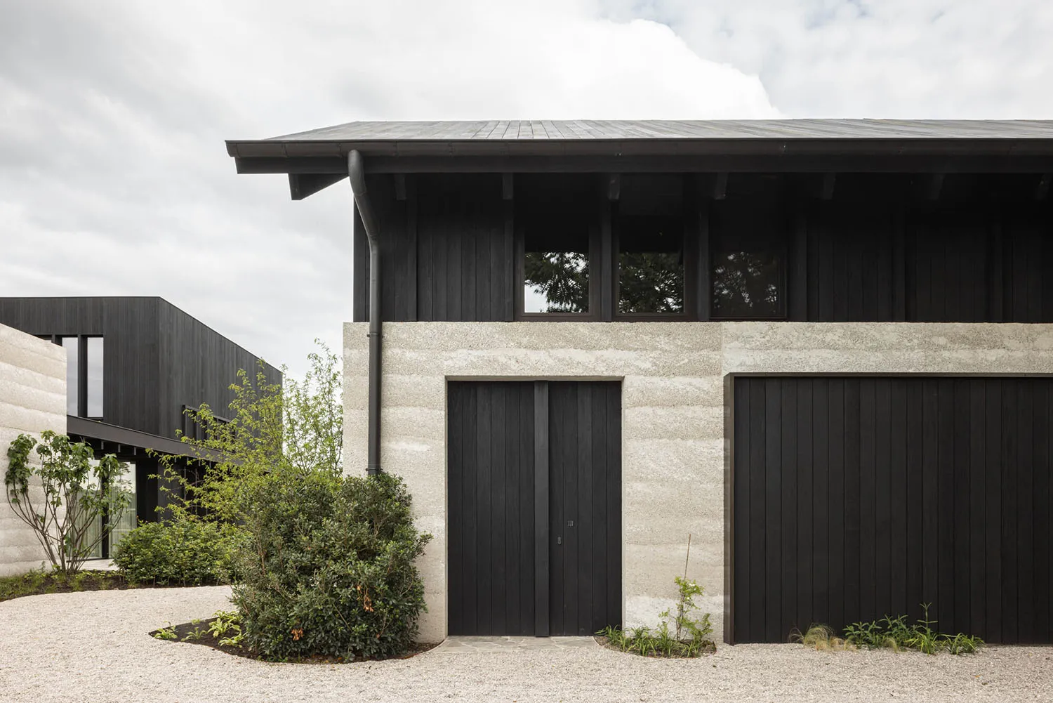 Black and concrete modern architectural exterior with black windows and doors, surrounded by gravel and green shrubs.