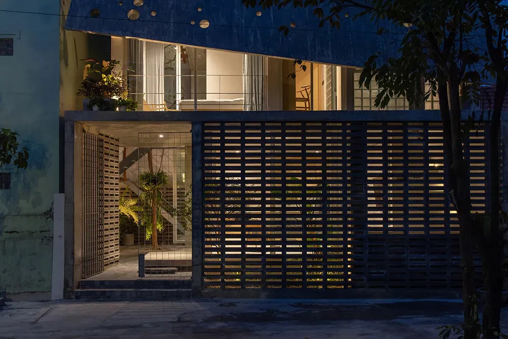Modern house exterior featuring concrete walls with a grid pattern and illuminated windows at night.