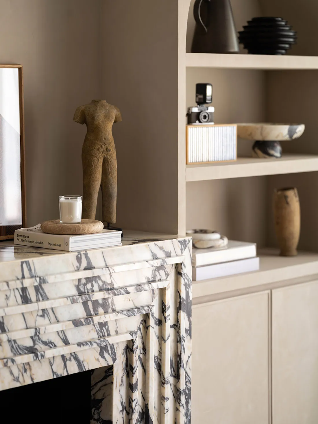 A modern living room featuring a marble fireplace and bookshelf filled with decorative items.