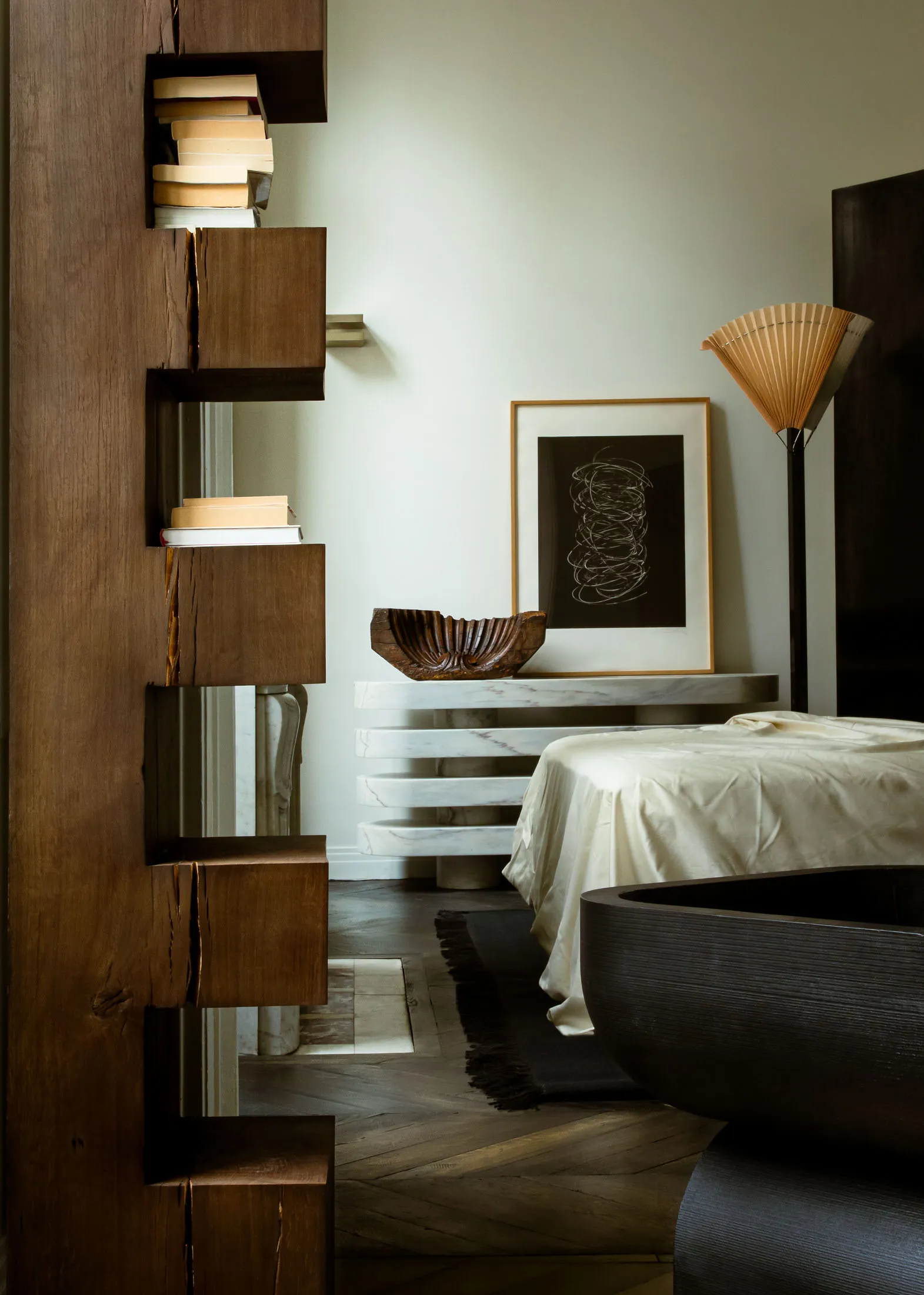 A modern minimalist bedroom featuring a white marble table, a wooden bookshelf, and a dark wood bathtub.