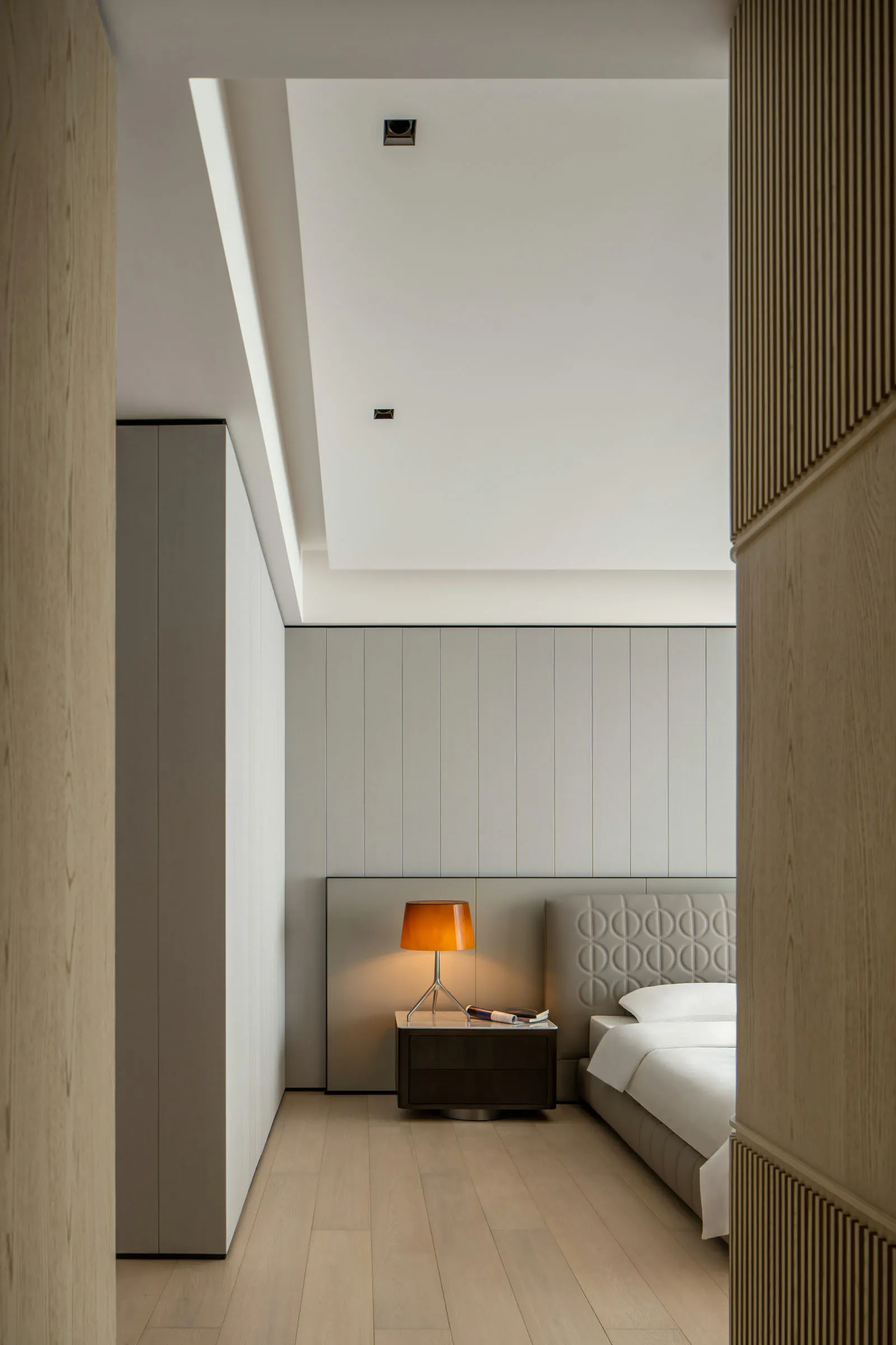 Minimalist bedroom with wooden paneling and a modern light fixture.