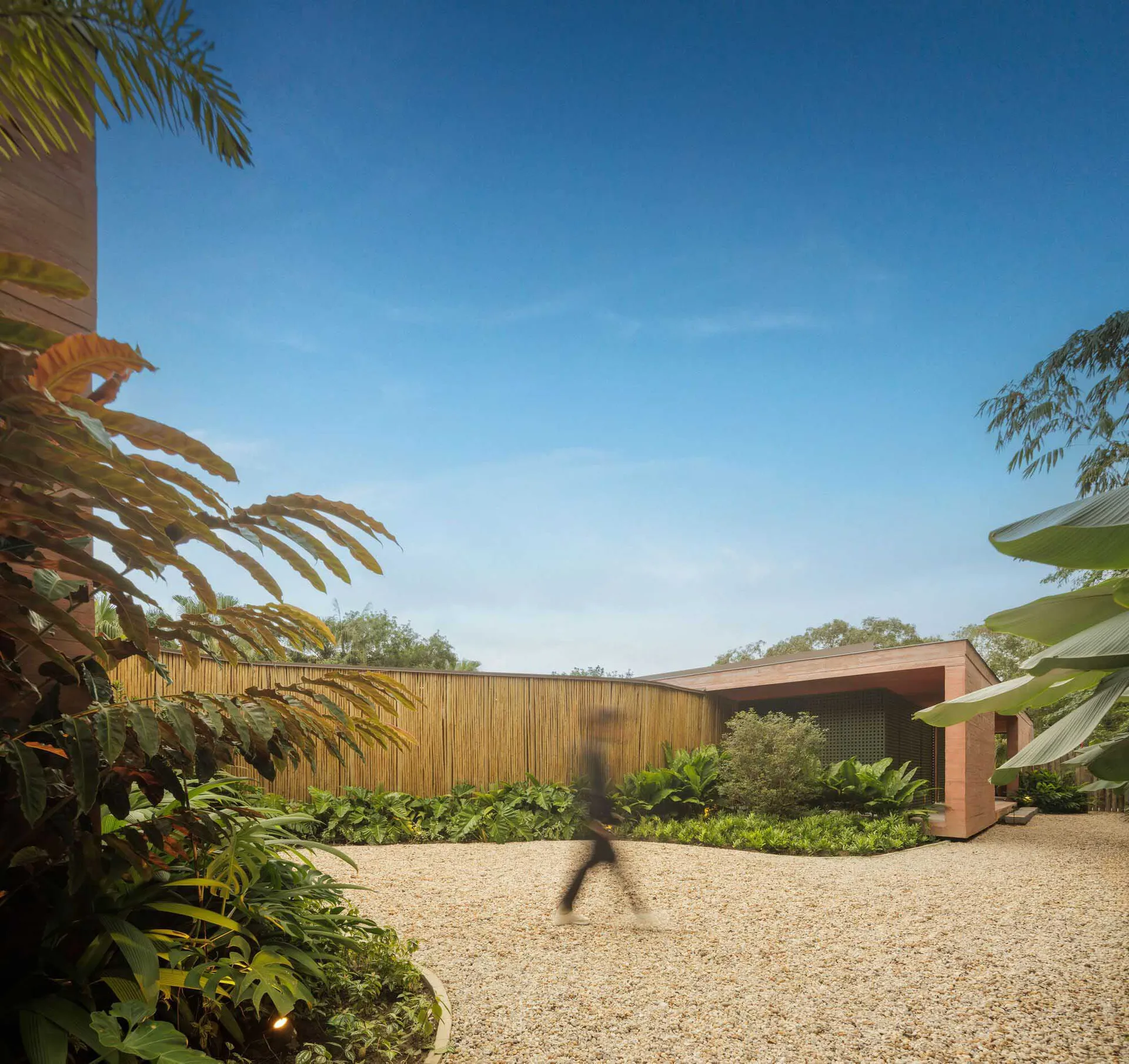 A modern residential building with a wooden exterior surrounded by lush greenery and a gravel driveway.