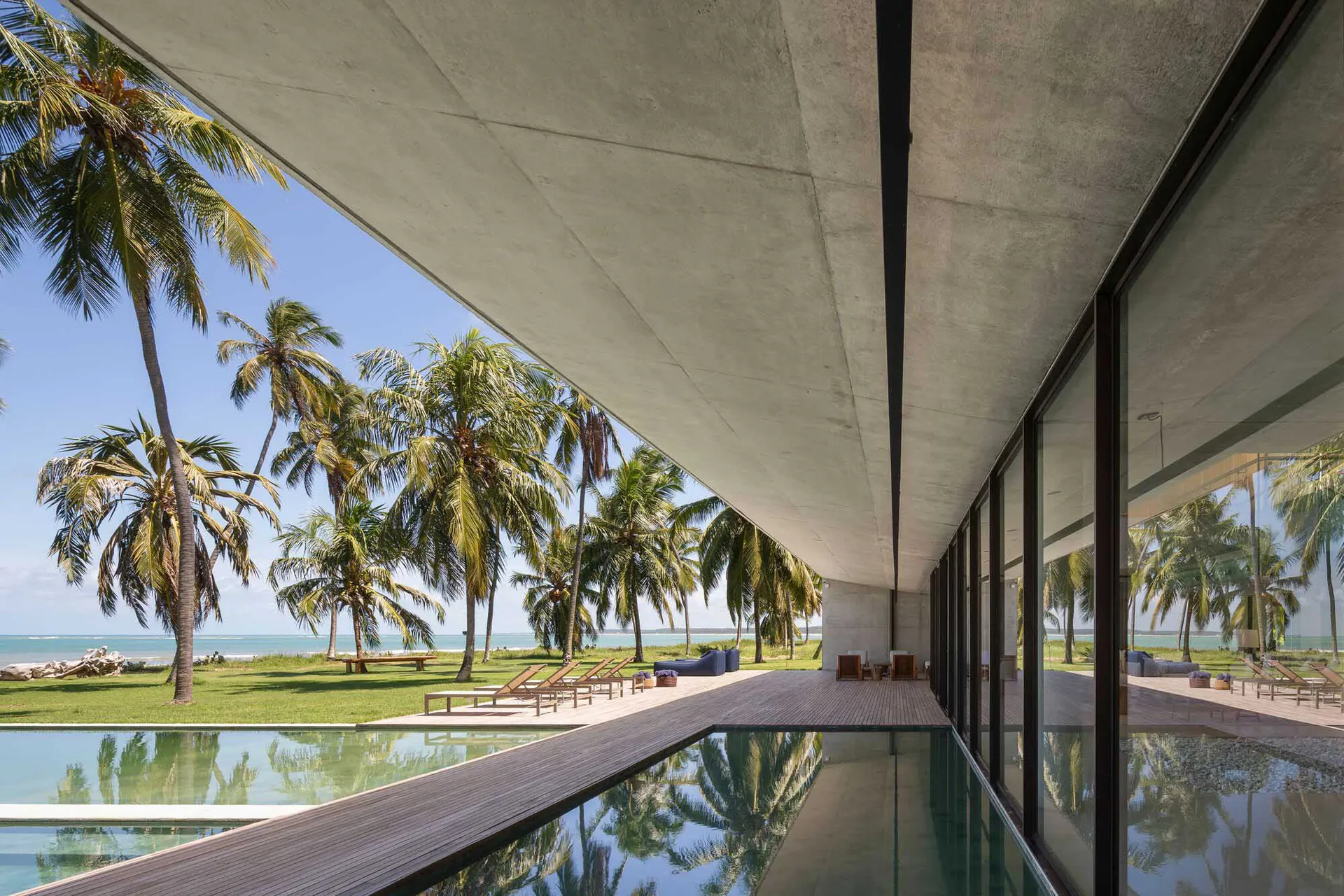 Modern residential interior with concrete walls, large glass windows, and wooden flooring.