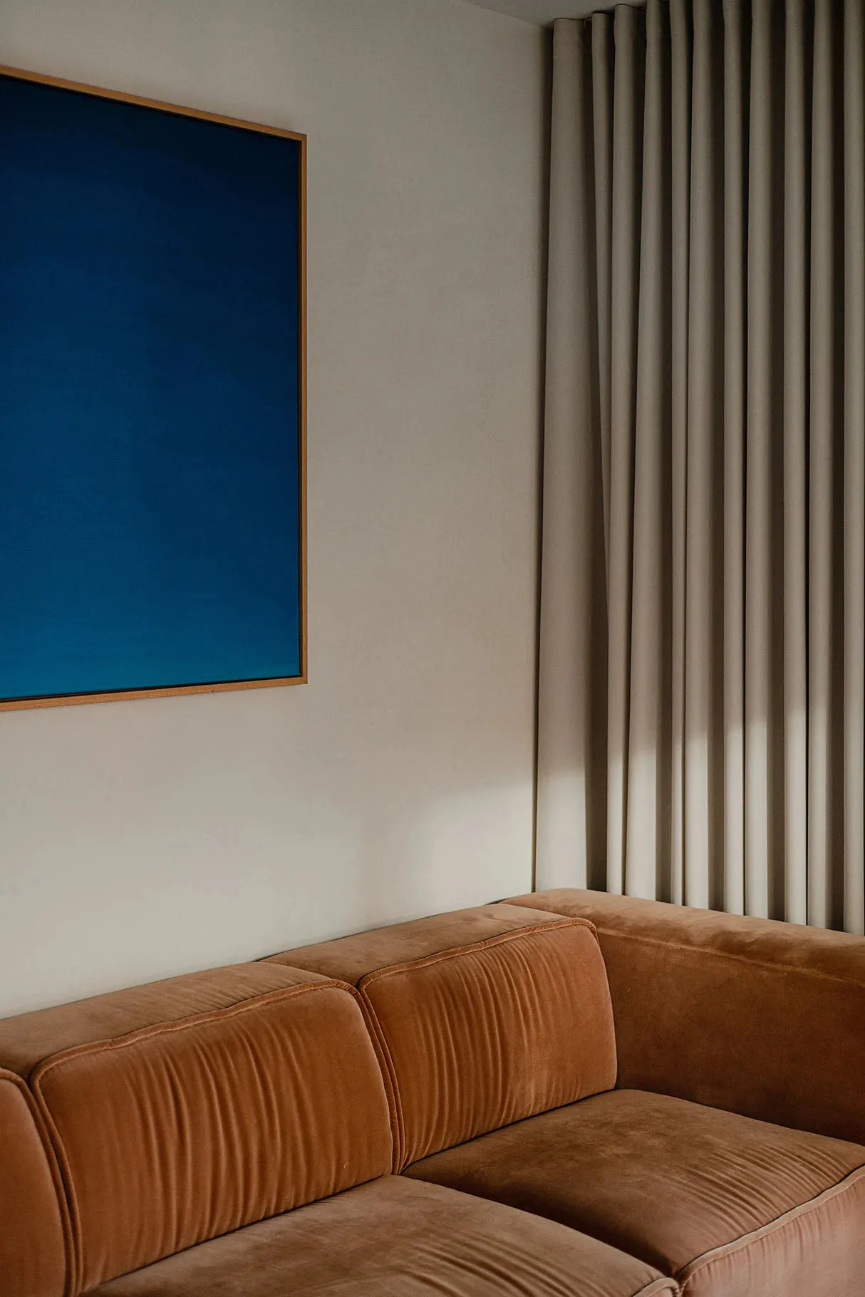 Modern sitting room featuring a brown velvet sofa and a blue artwork on the wall.