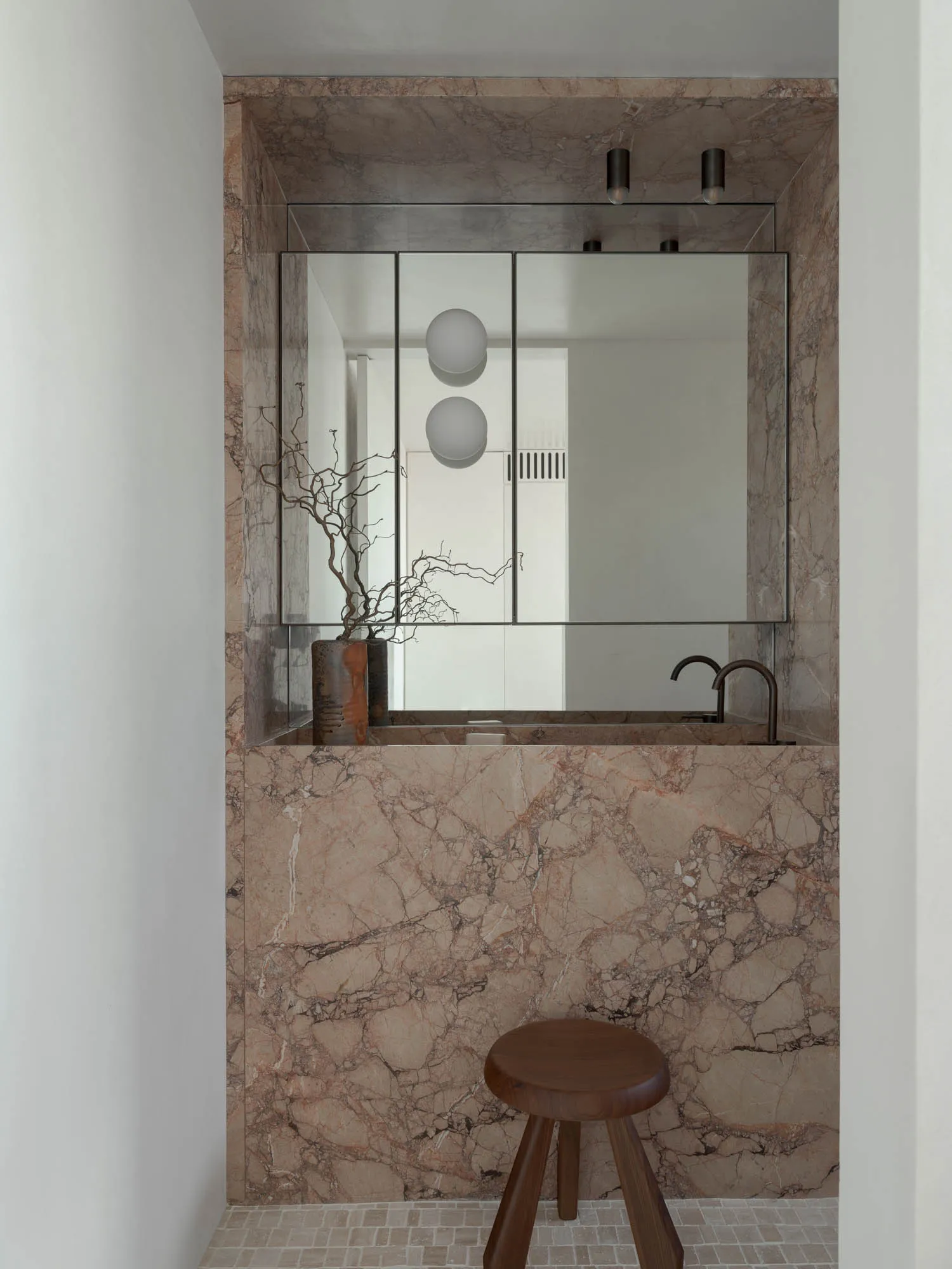 Modern bathroom with marble walls and floor, featuring a sink with a faucet and a round wooden stool.