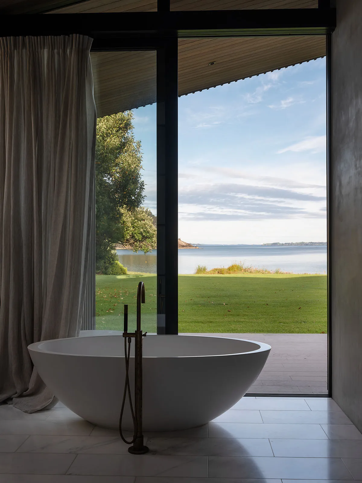 A minimalist bathroom featuring a freestanding bathtub with a beautiful coastal view through large windows.