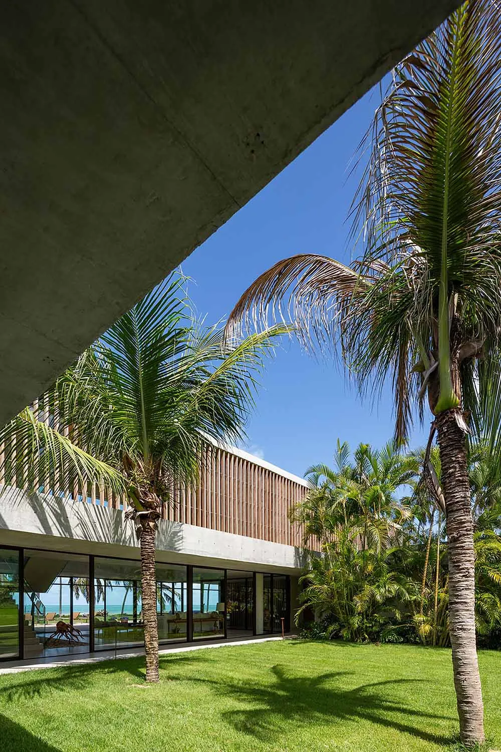 Modern minimalist house exterior featuring concrete and glass materials under a clear blue sky.