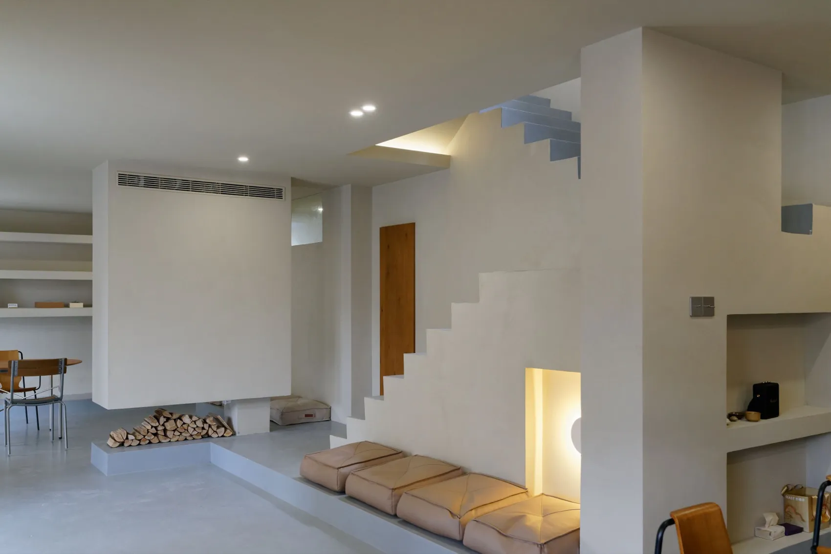 A minimalistic, modern living room with concrete walls and floors, featuring a fireplace and seating area.