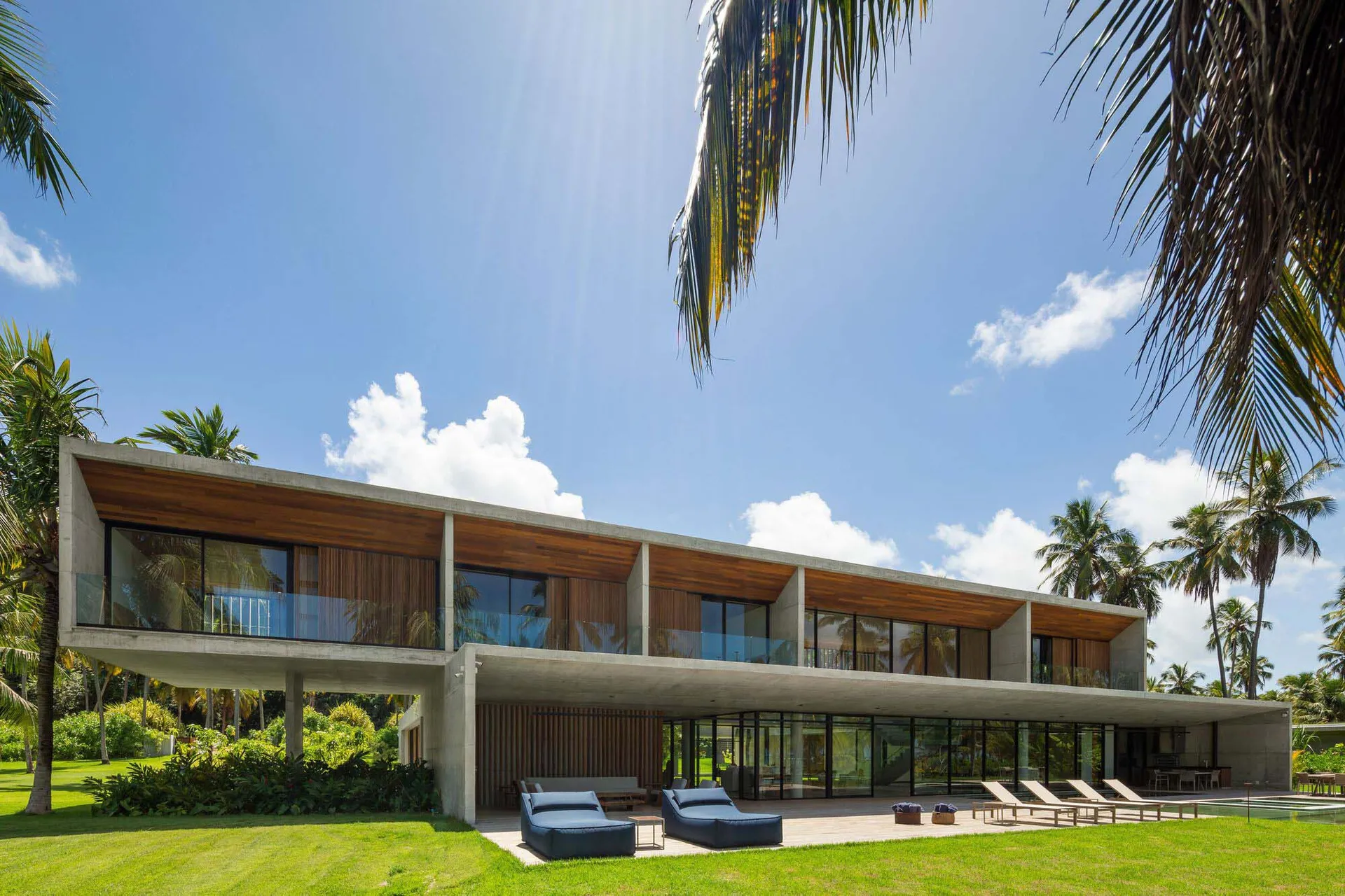 A modern house with concrete and glass materials, featuring a spacious outdoor area with lounge chairs and a pool.
