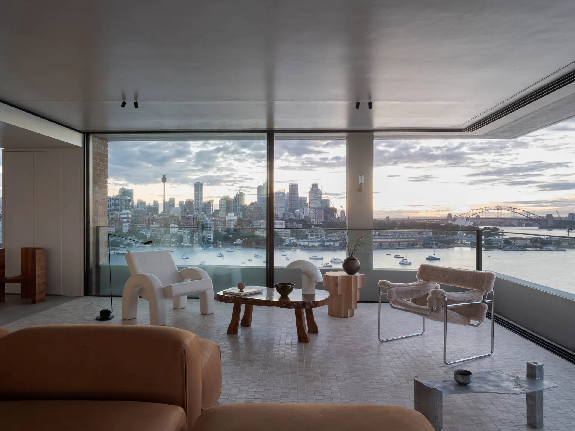 A modern living room with a view of the cityscape and water, featuring minimalist furniture and sleek design elements.