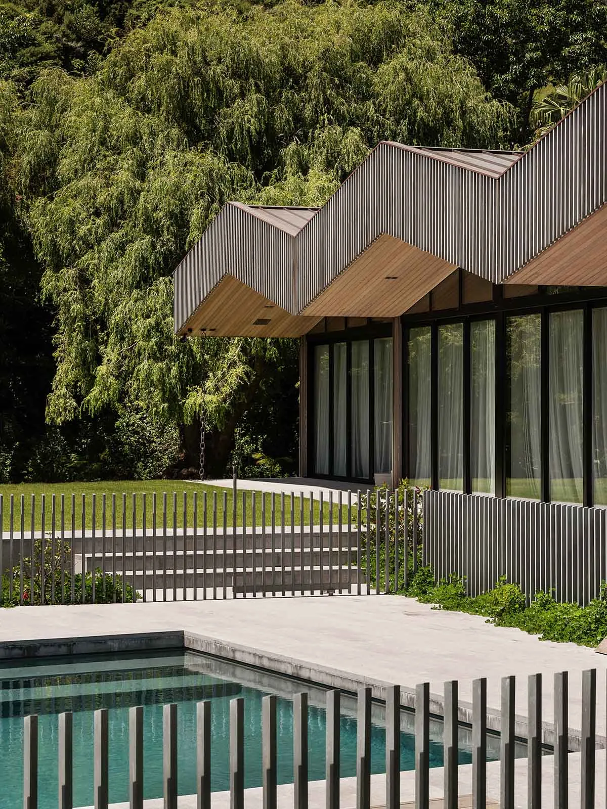 Modern minimalistic house featuring concrete exterior walls, a swimming pool with a metal fence, and a lush green courtyard w