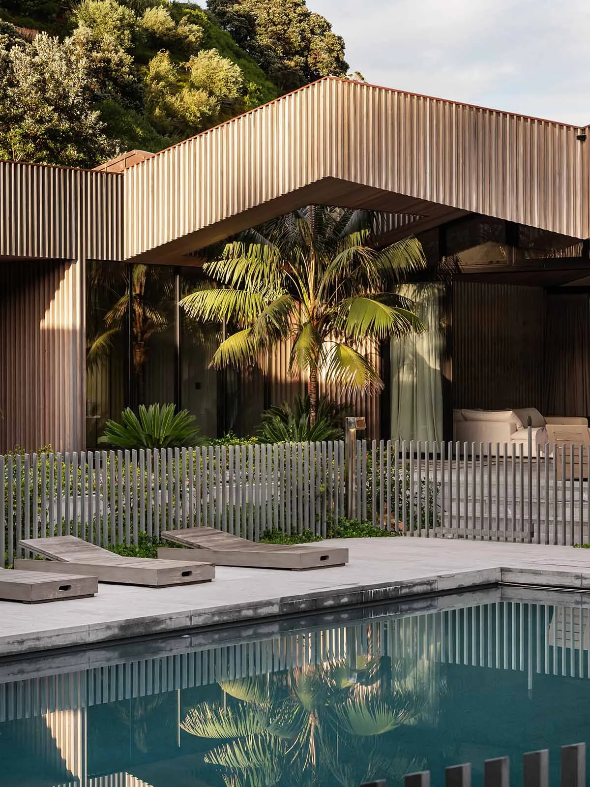 A modern residential exterior featuring wood siding and a pool area with lounge seating.