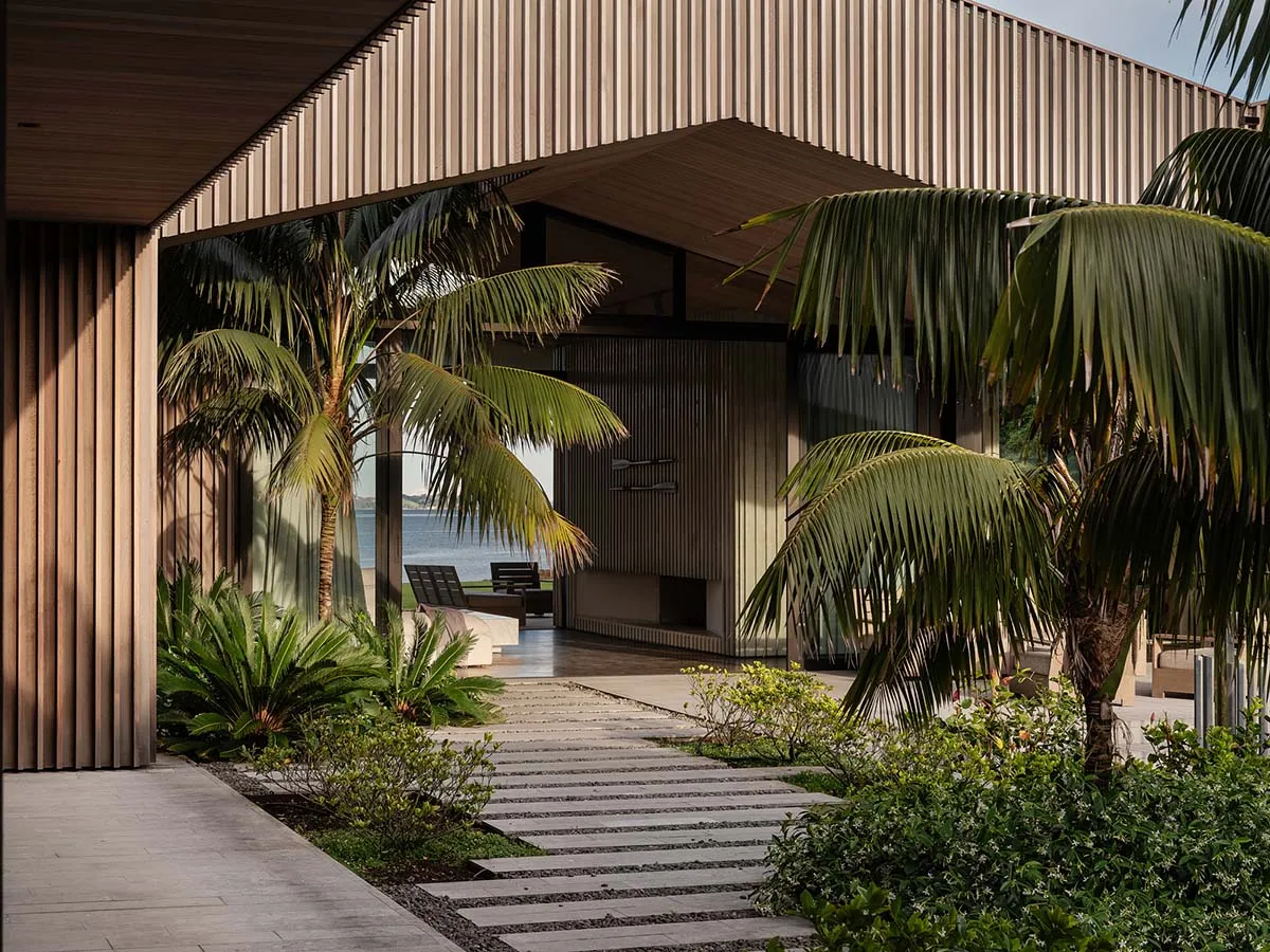 現代住宅庭院,鋪設石板步道、木質牆板,並有棕櫚樹眺望大海。