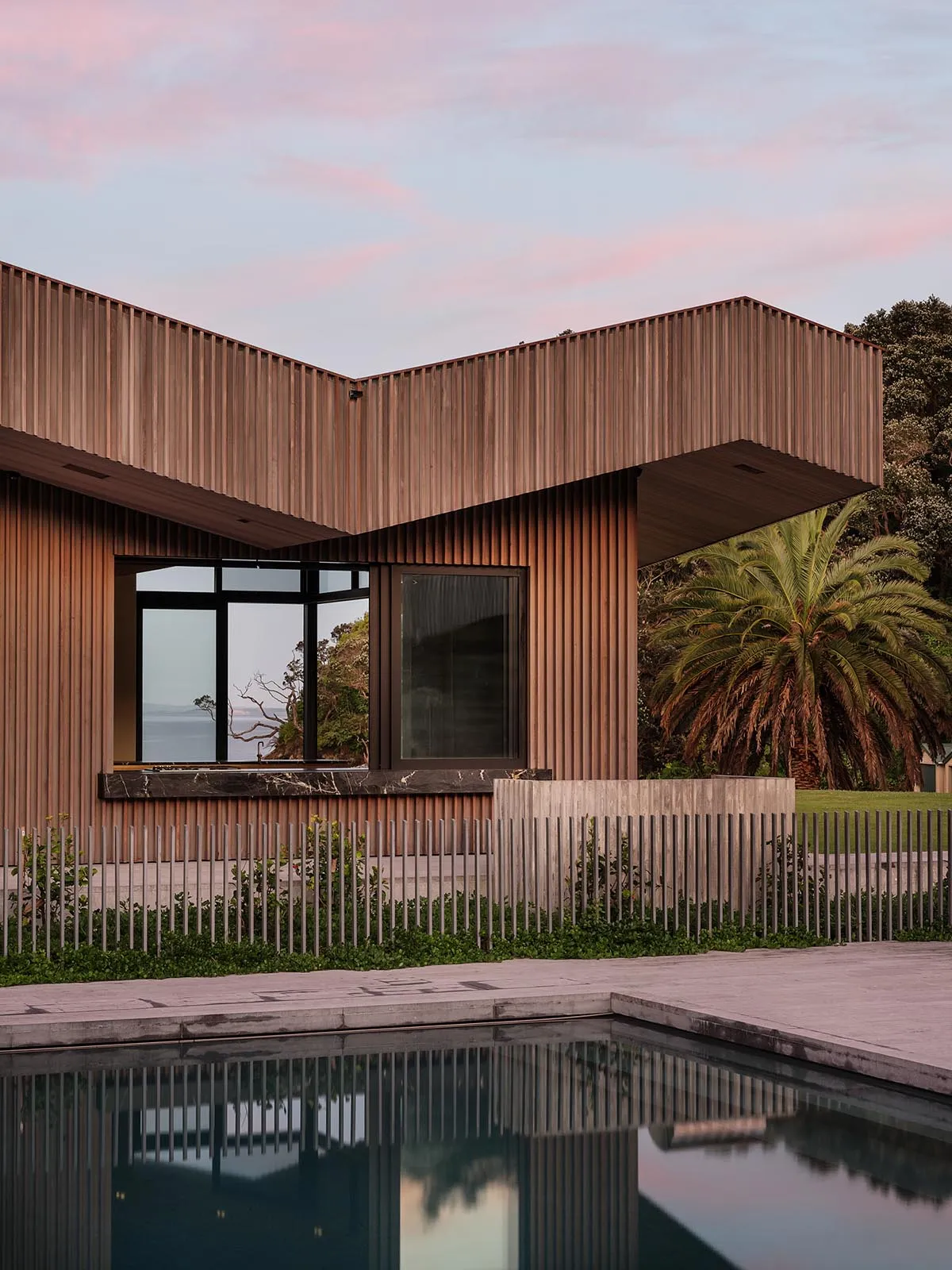 A modern residential house with wooden exterior and large windows, featuring a pool and landscaped garden.