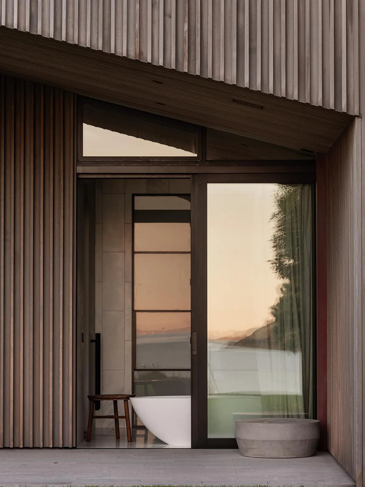 Modern bathroom with large glass door, concrete floor, and wooden paneling.