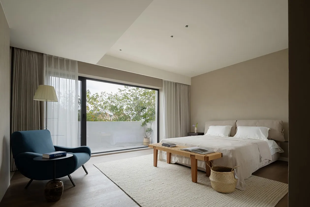 A modern minimalist bedroom with white walls, a neutral color palette, and a large window with curtains.