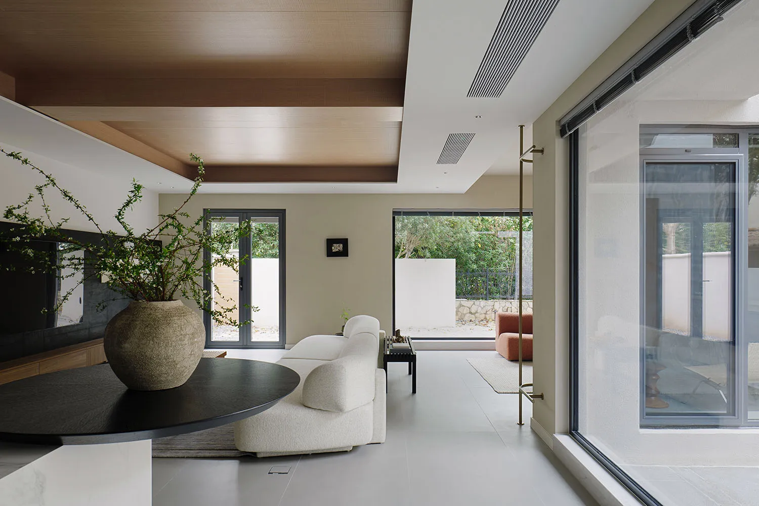 Modern minimalist living room with white upholstered furniture, marble flooring, and large windows overlooking greenery.