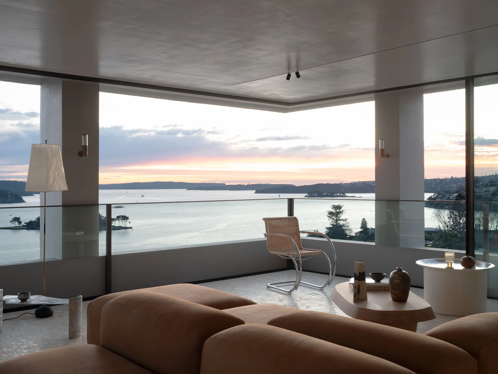 A minimalist living room featuring a modern leather sofa, a glass coffee table with ceramic ornaments, and a view of the sea