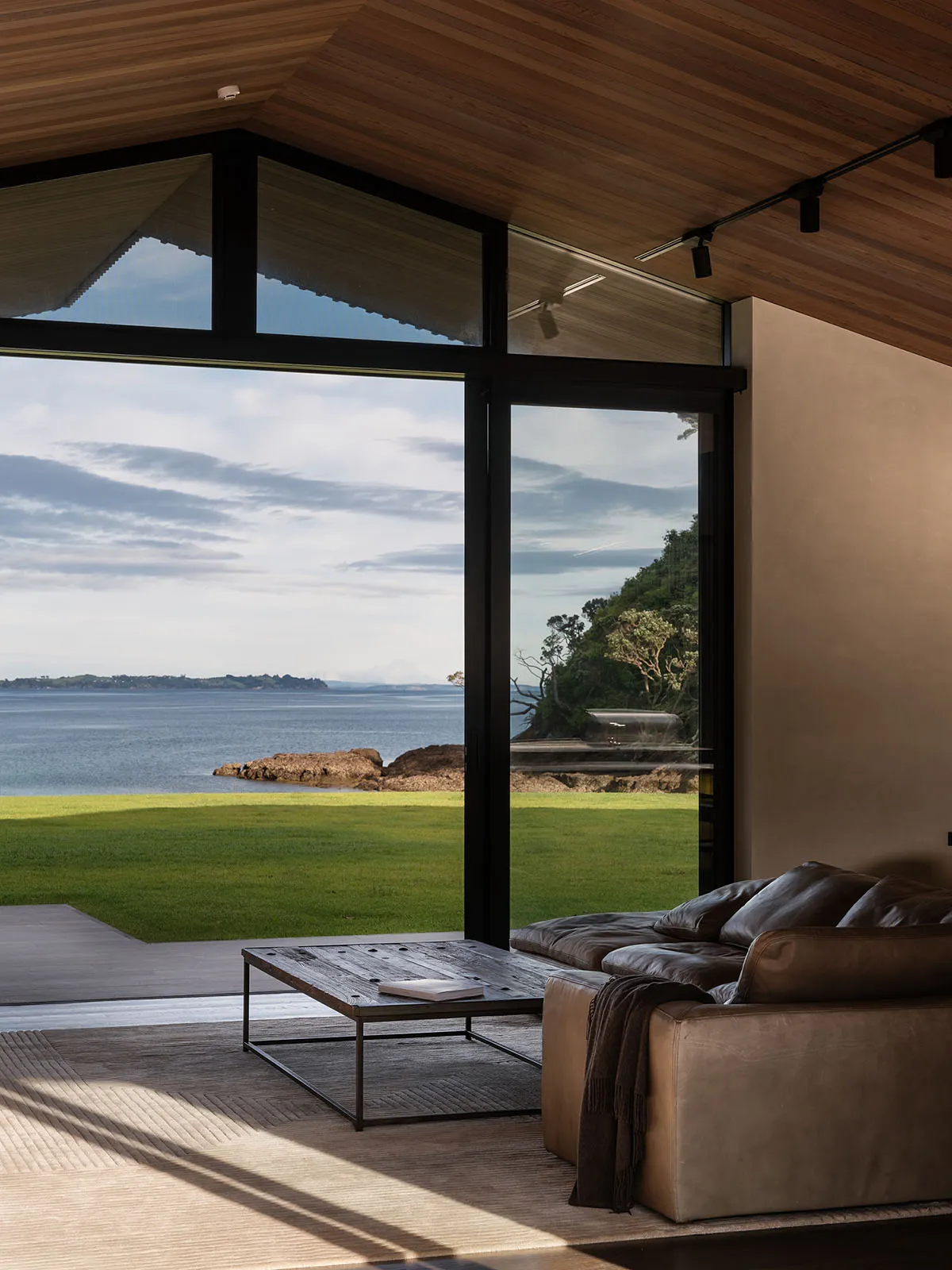 Modern living room featuring glass windows, wooden flooring, and a cozy leather sofa.