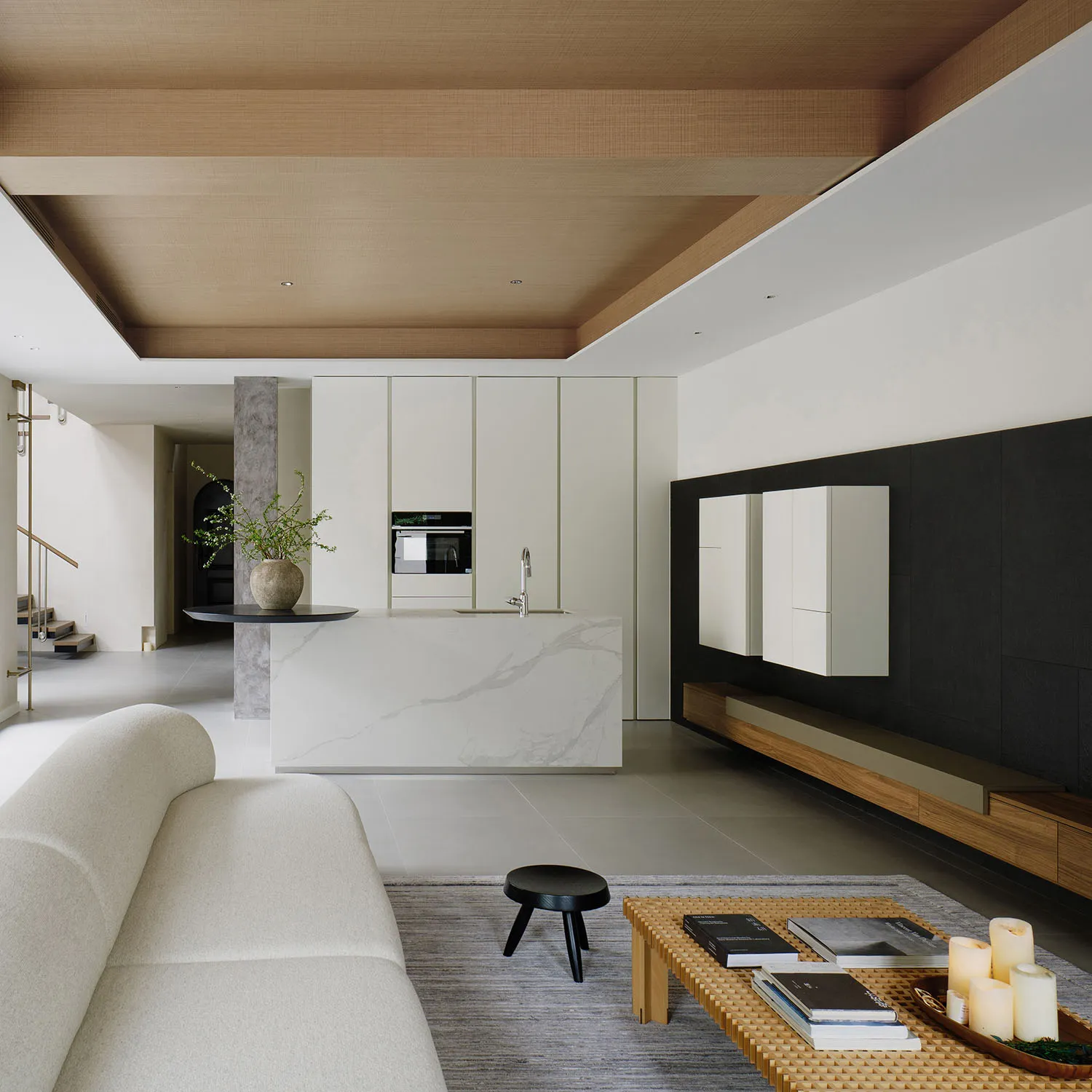 A modern living room featuring a white couch, a coffee table with candles and books, and a kitchen island with a marble count