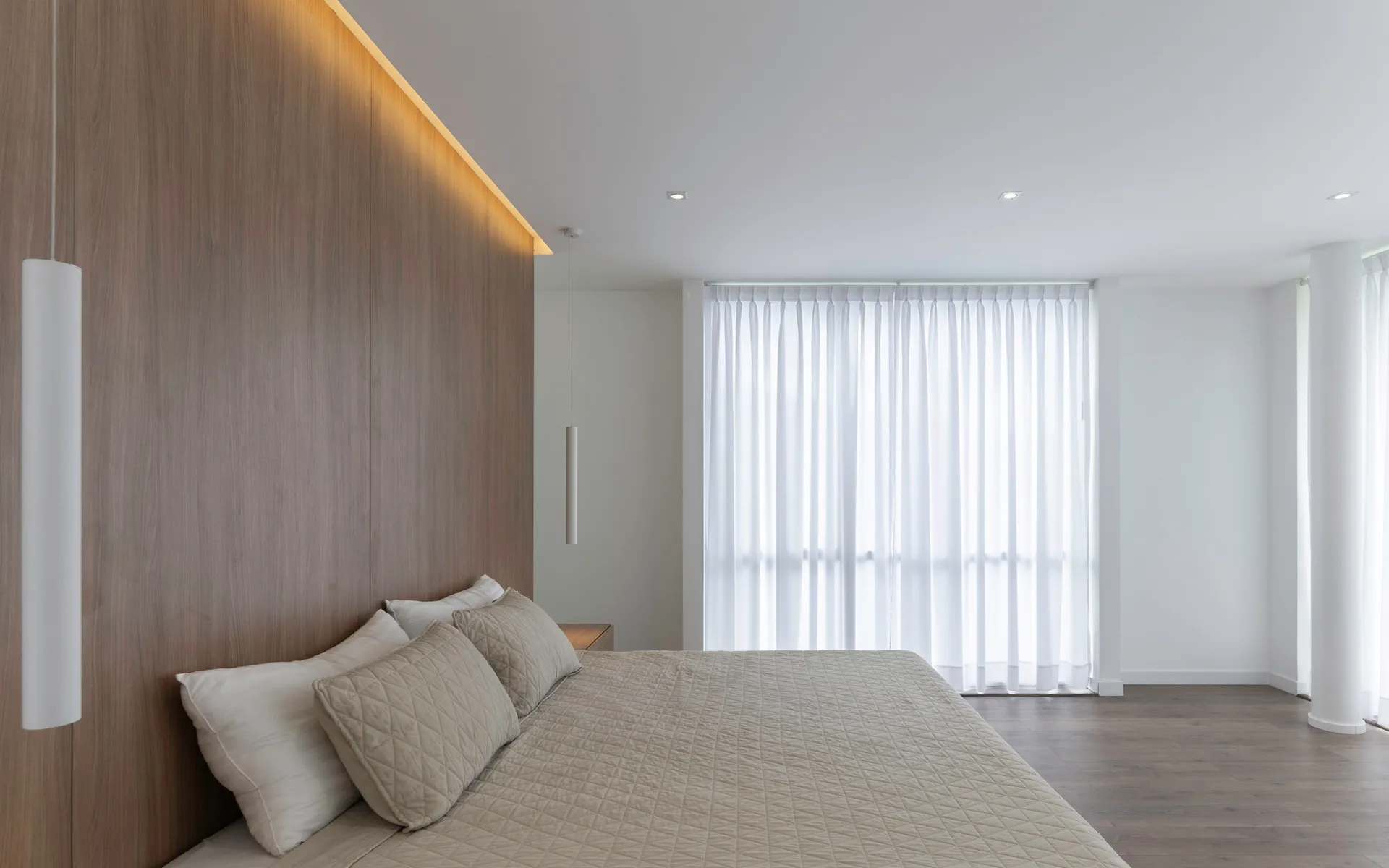 Modern minimalist bedroom with textured cotton blanket, white curtains, gray floor, and wood headboard.