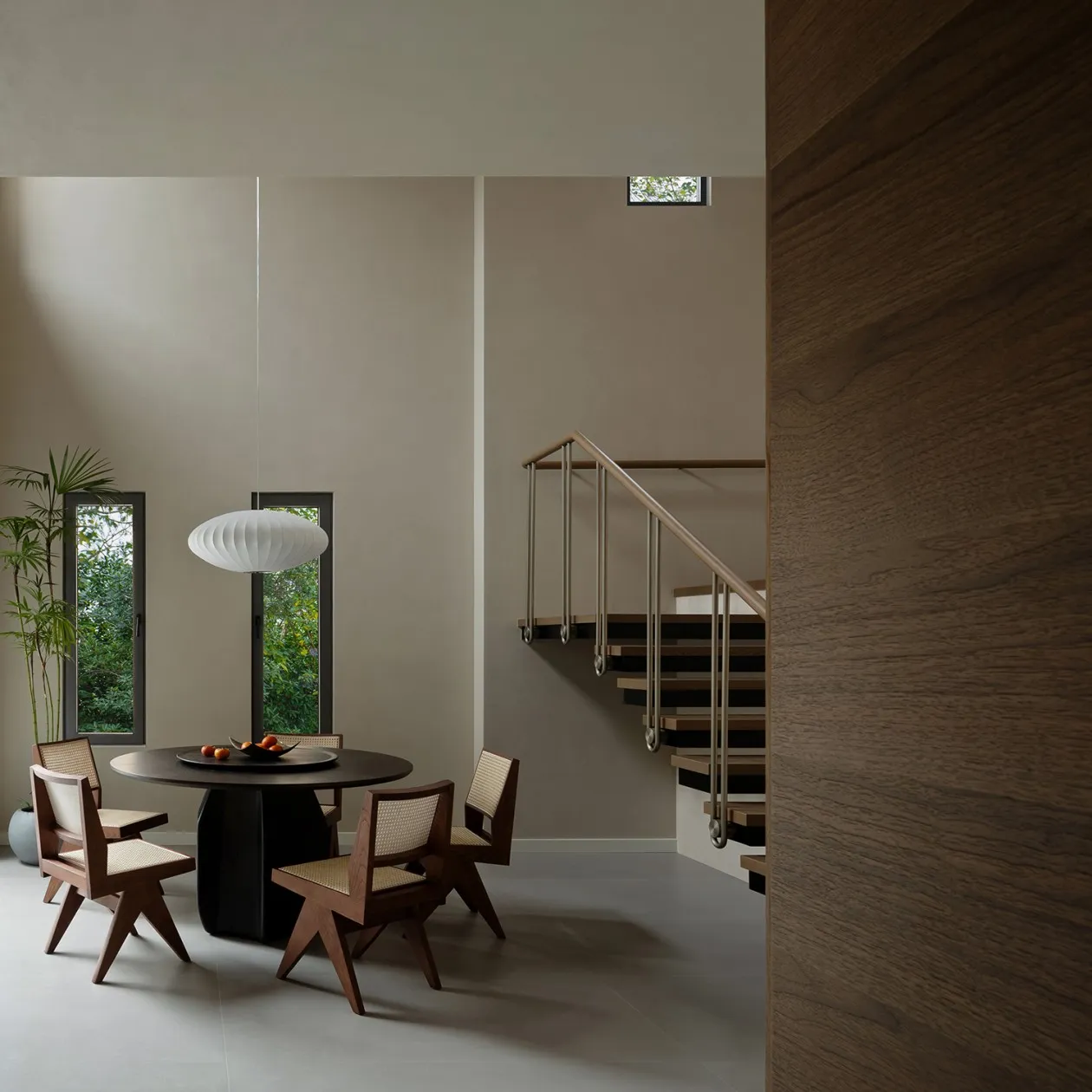 A modern minimalist dining room featuring a wooden table and chairs with a white pendant light hanging above it, set against