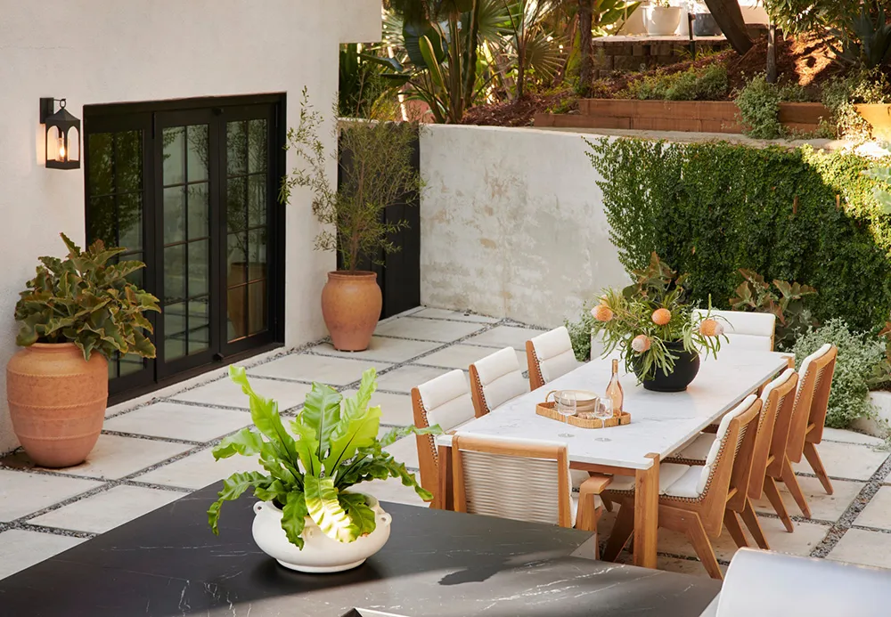 Outdoor dining terrace featuring marble dining table, concrete floor, wooden chairs, and terracotta planters with greenery.