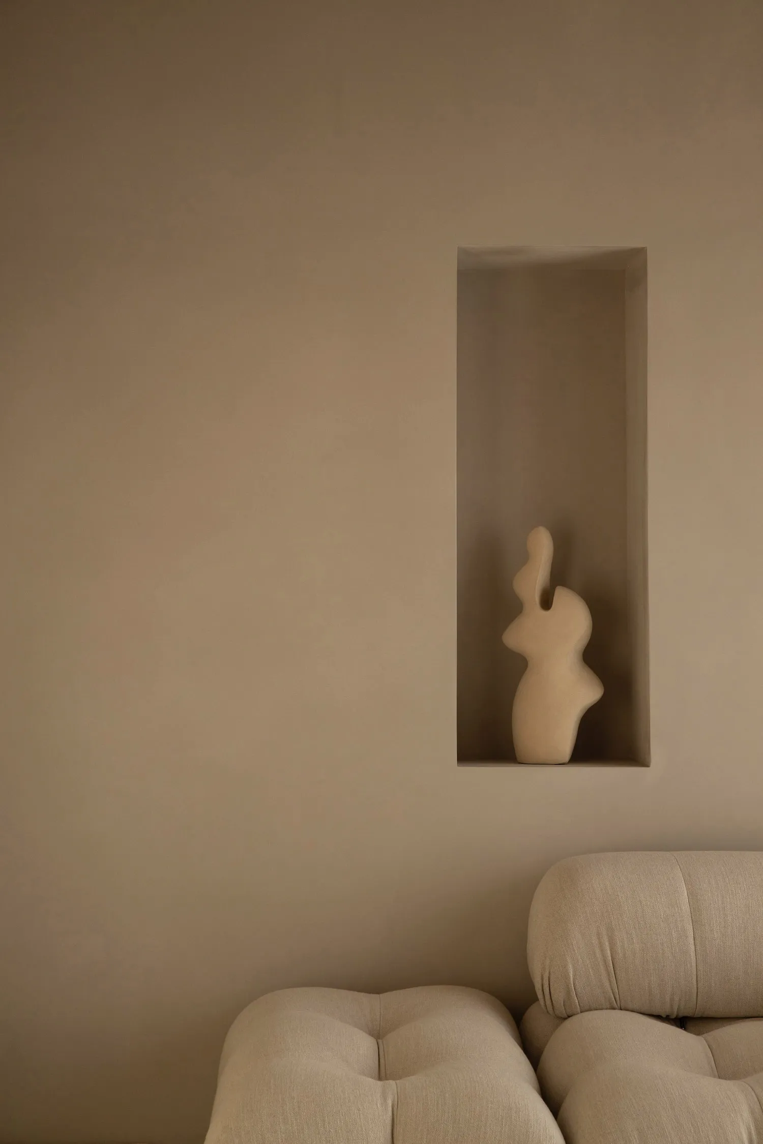 A minimalist brown ceramic vase displayed on a recessed concrete shelf.