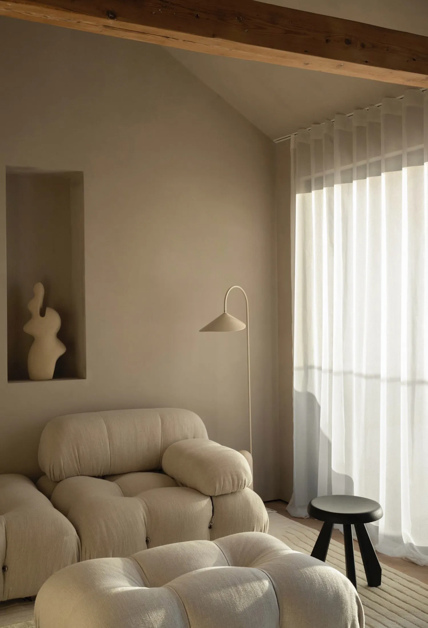 A minimalist living room features a fabric sofa, curtains, and a stool.