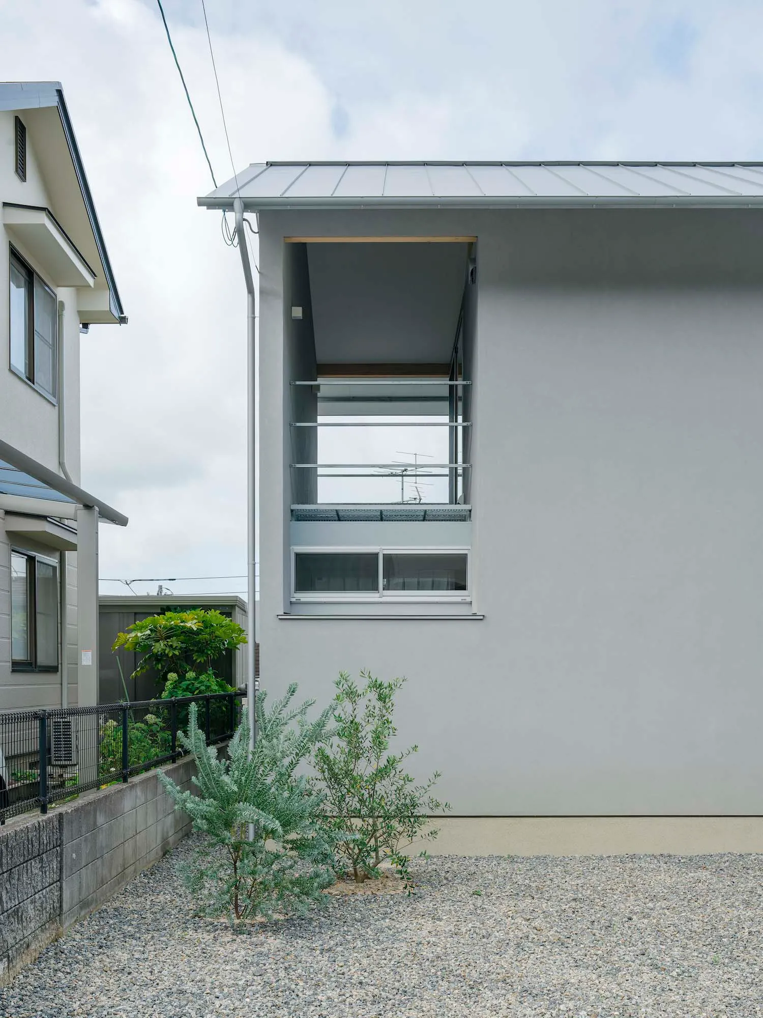Modern residential house with concrete cladding exterior, small garden area with gravel and greenery, and minimalist architec