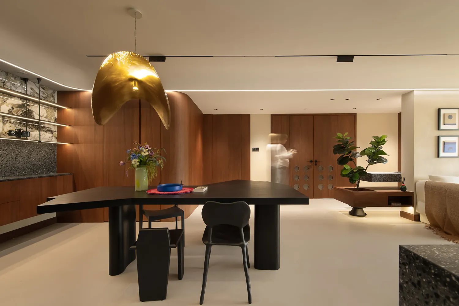 A modern dining room featuring wooden walls and furniture, with a distinctive golden pendant light hanging above a sleek dini