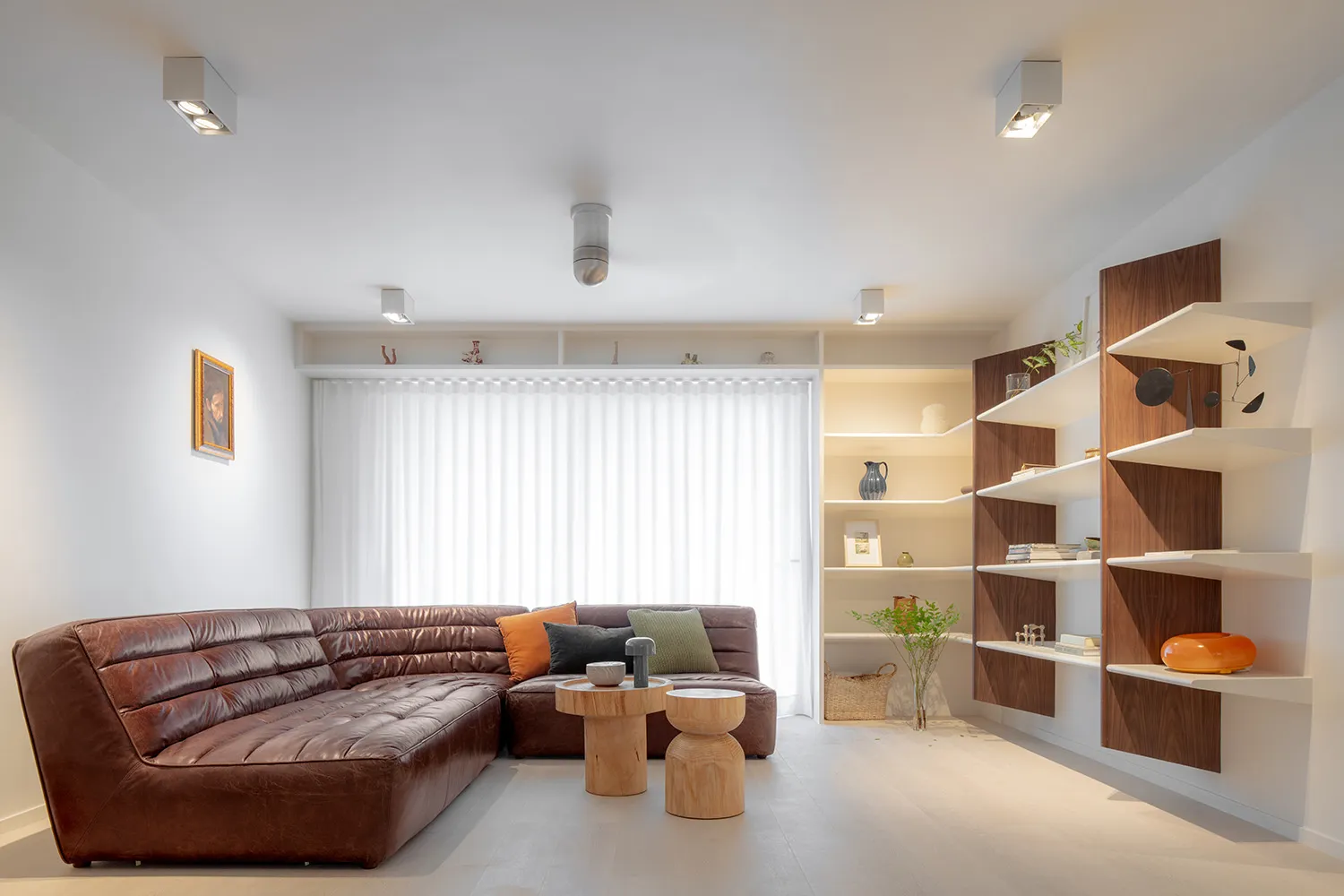 Modern living room featuring a brown leather sofa, white curtains, and wooden shelving.