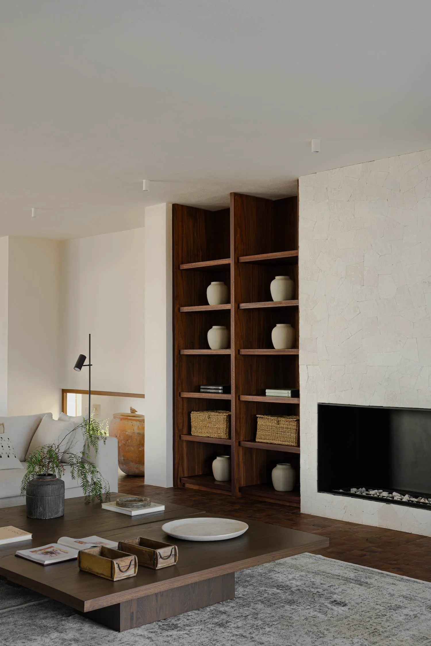 Modern living room with wooden shelves, ceramic vases, and stone fireplace