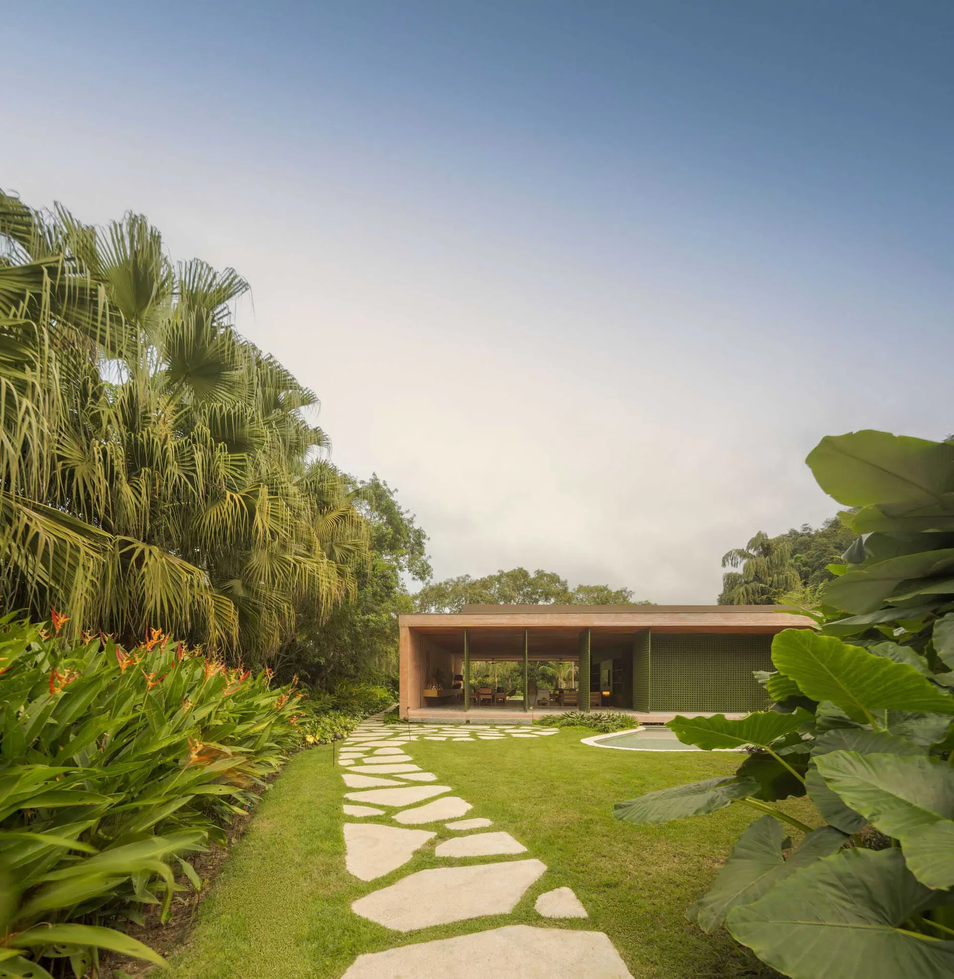 A modern residential exterior with a stone pathway and tropical garden.