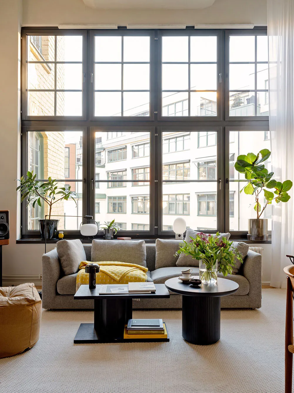 A modern, minimalist living room with a large window, a gray sofa, and a black coffee table.