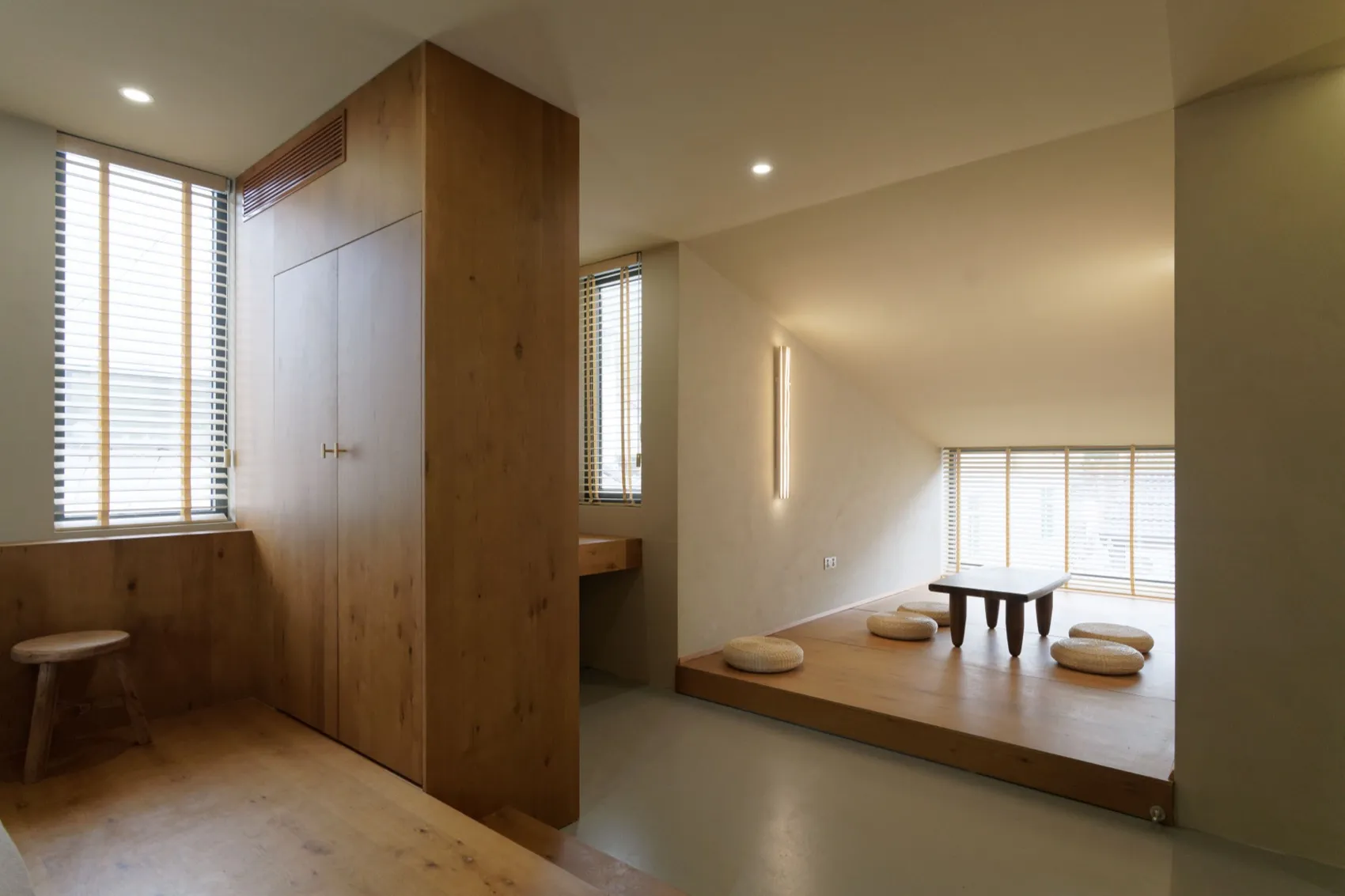 A minimalist living space featuring wooden furniture and flooring, with a low table and cushions for seating.