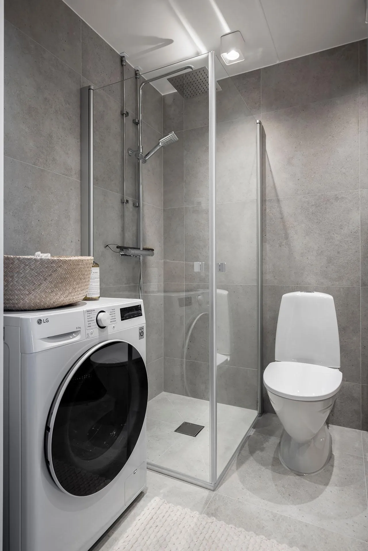 Modern bathroom with concrete walls, glass shower enclosure, washing machine, and toilet.