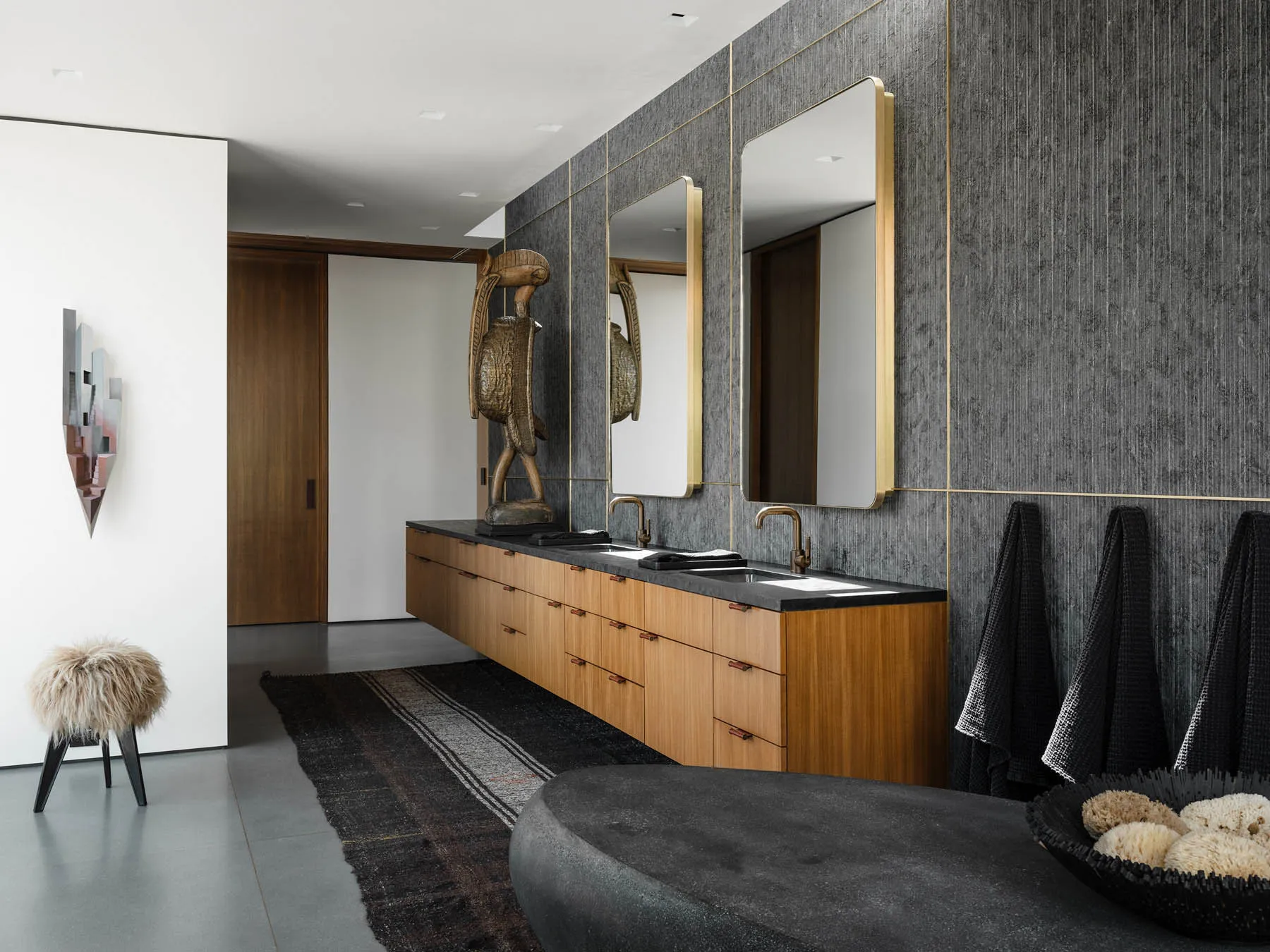 Modern bathroom with wooden vanity, black marble countertop, metallic faucets, and textured grey walls.