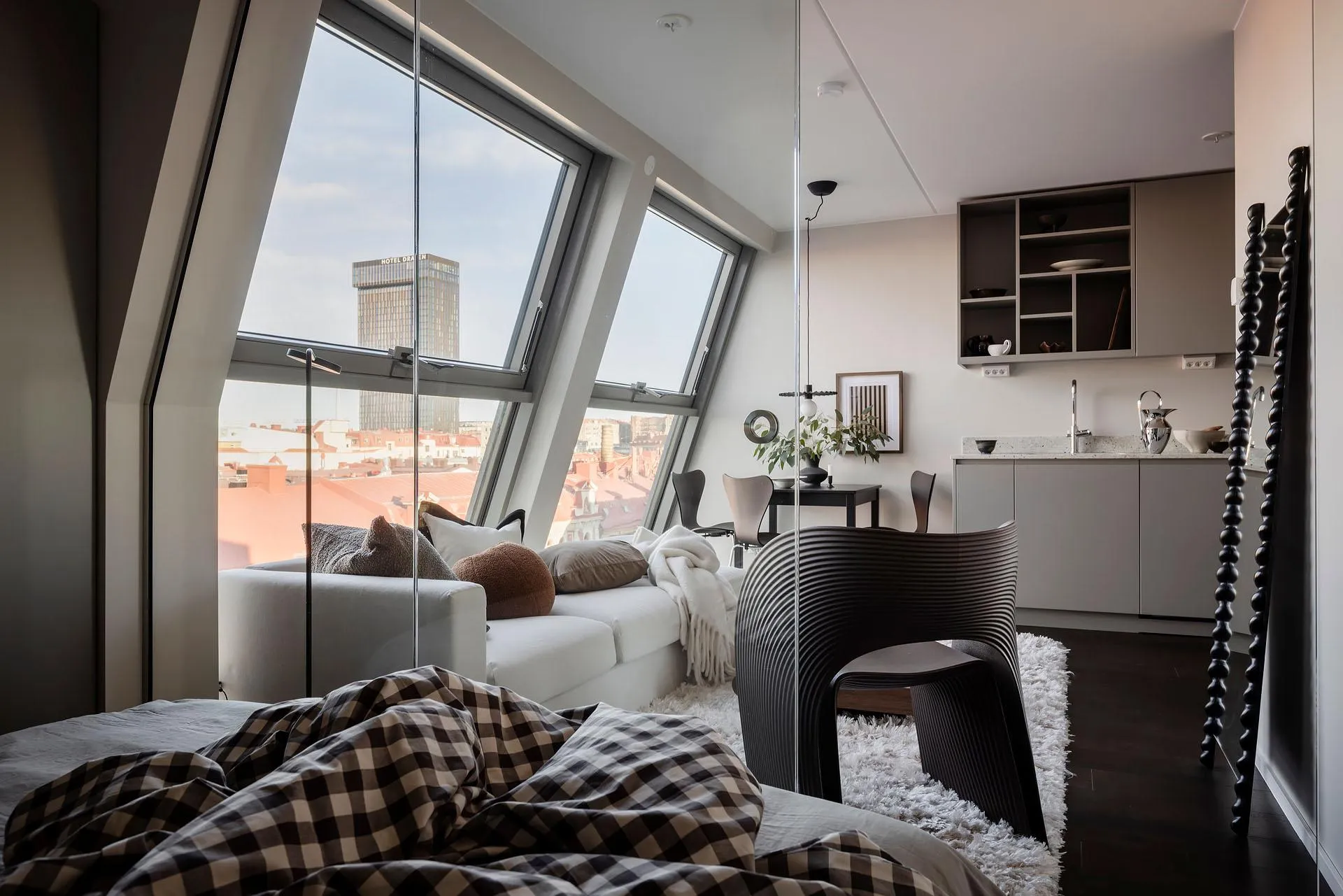 A modern apartment loft featuring a living space with a white sofa, dark furniture, and large windows overlooking the citysca