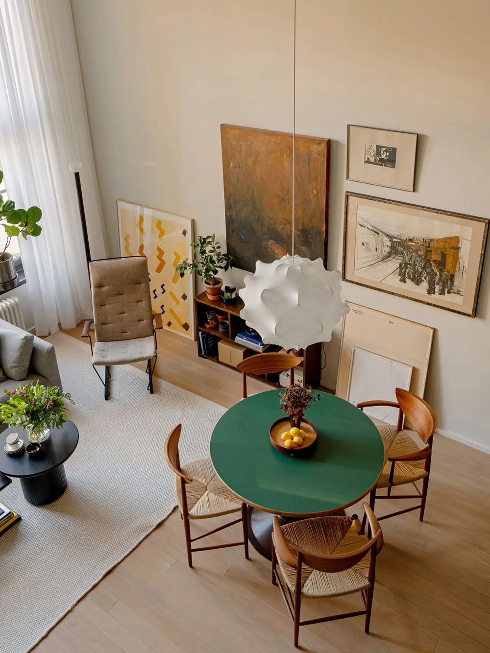 A modern living and dining room featuring wooden furniture and decor with art on the walls and a green table.