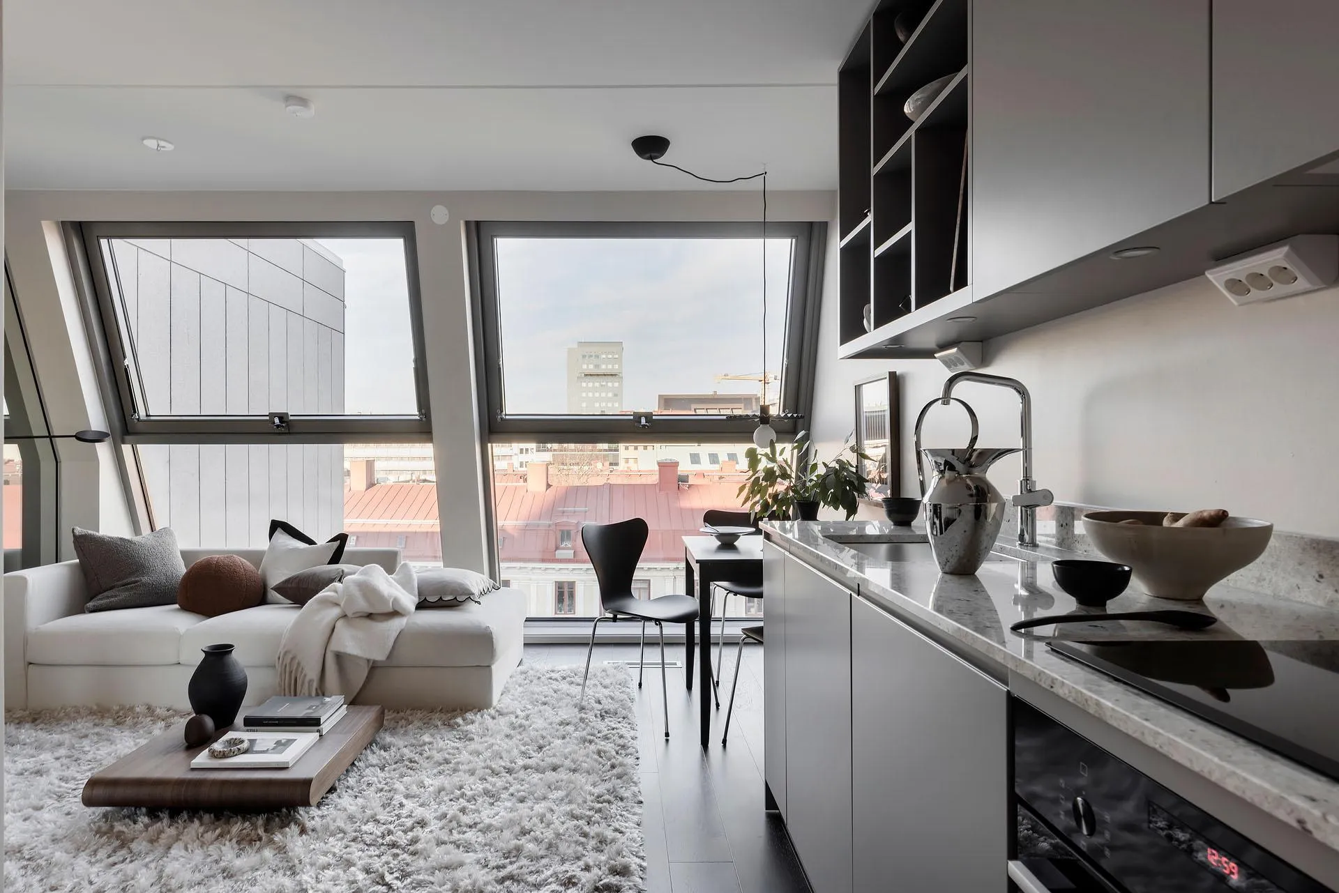 A modern living room with concrete, glass, and metal elements, featuring a white sofa, black chairs, and a minimalist design.
