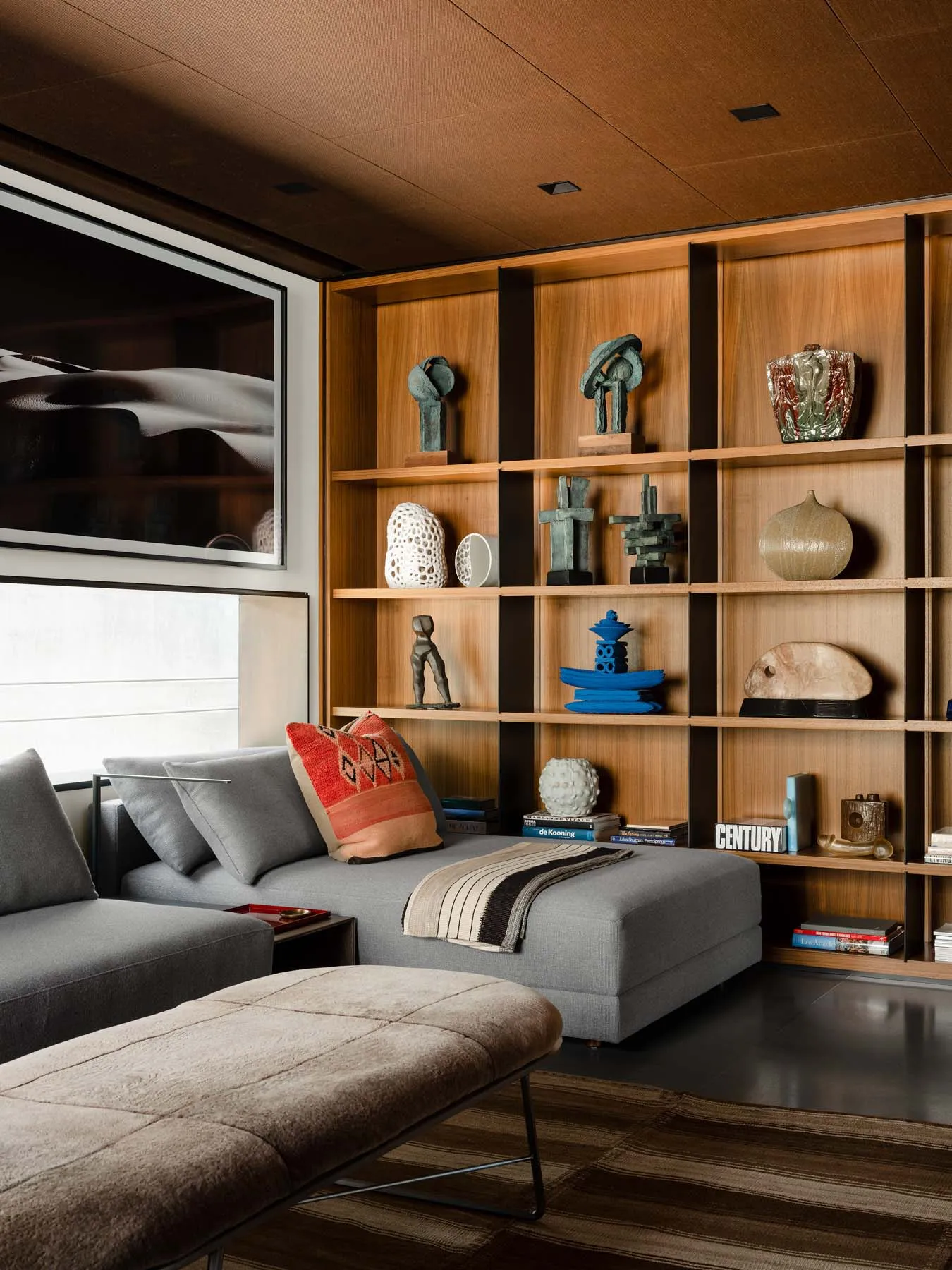 A modern living room featuring wooden shelves, glass sculptures, and metal accents, with a comfortable sofa and a unique rug.