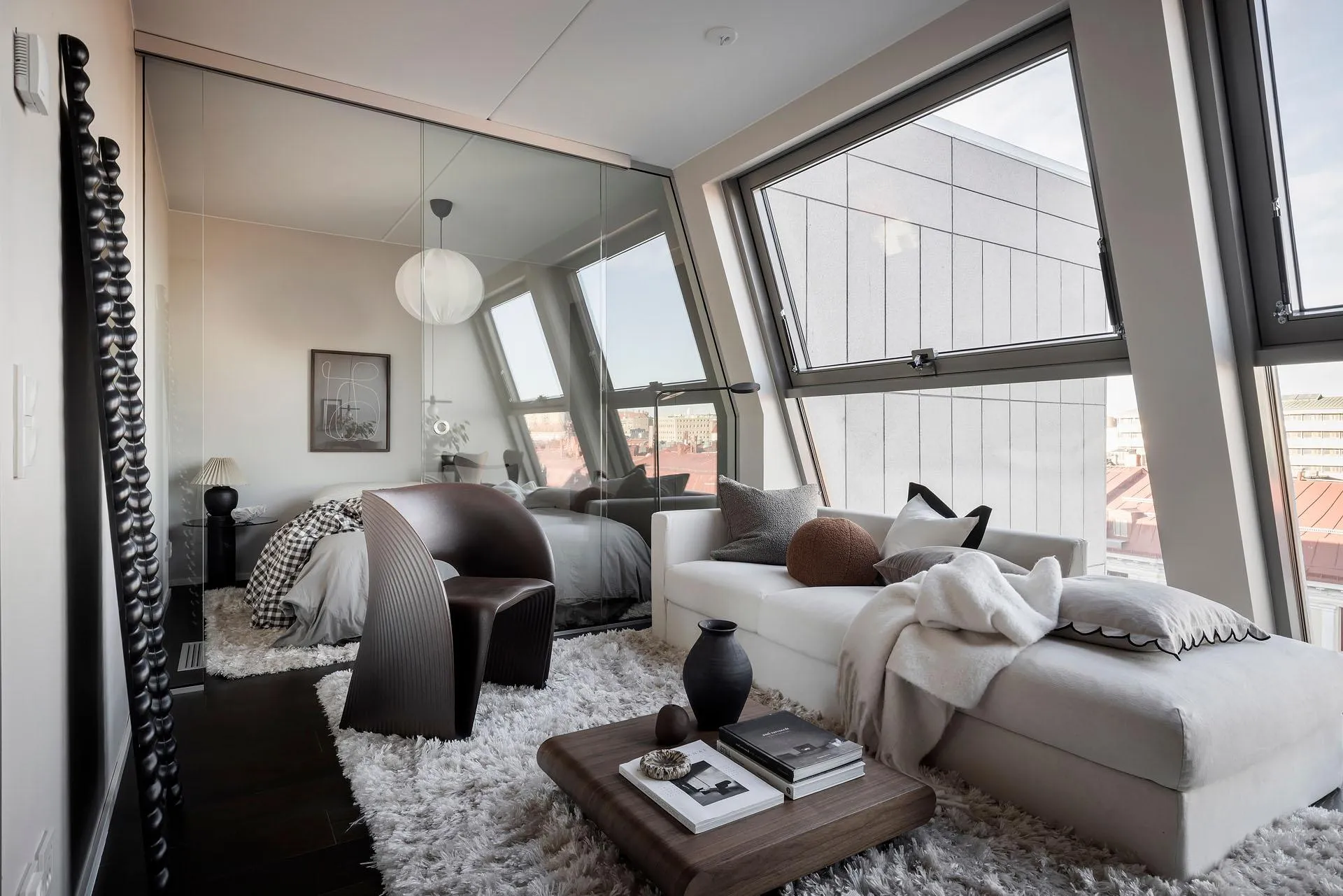 A modern minimalist living room featuring a white leather sofa, minimalist decor, and large windows with a view of the city.