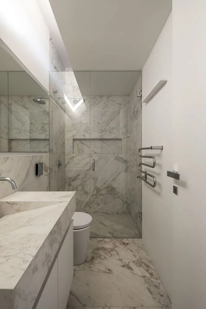 Modern minimalist bathroom with marble walls and floor, featuring a walk-in shower with glass door, a toilet, and a vanity si