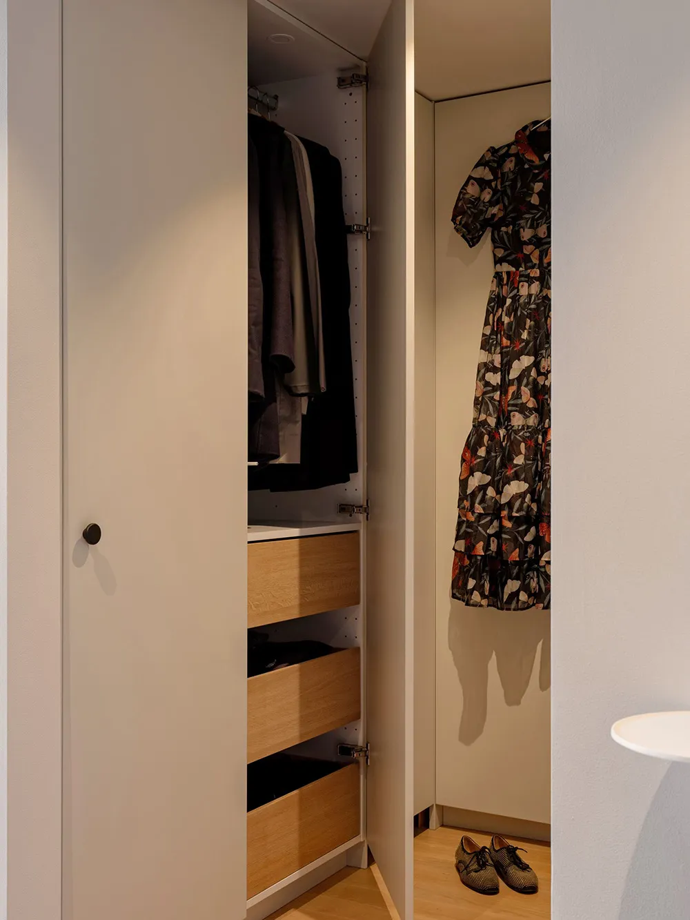 A modern white closet with wooden drawers and a floral dress hanging inside.