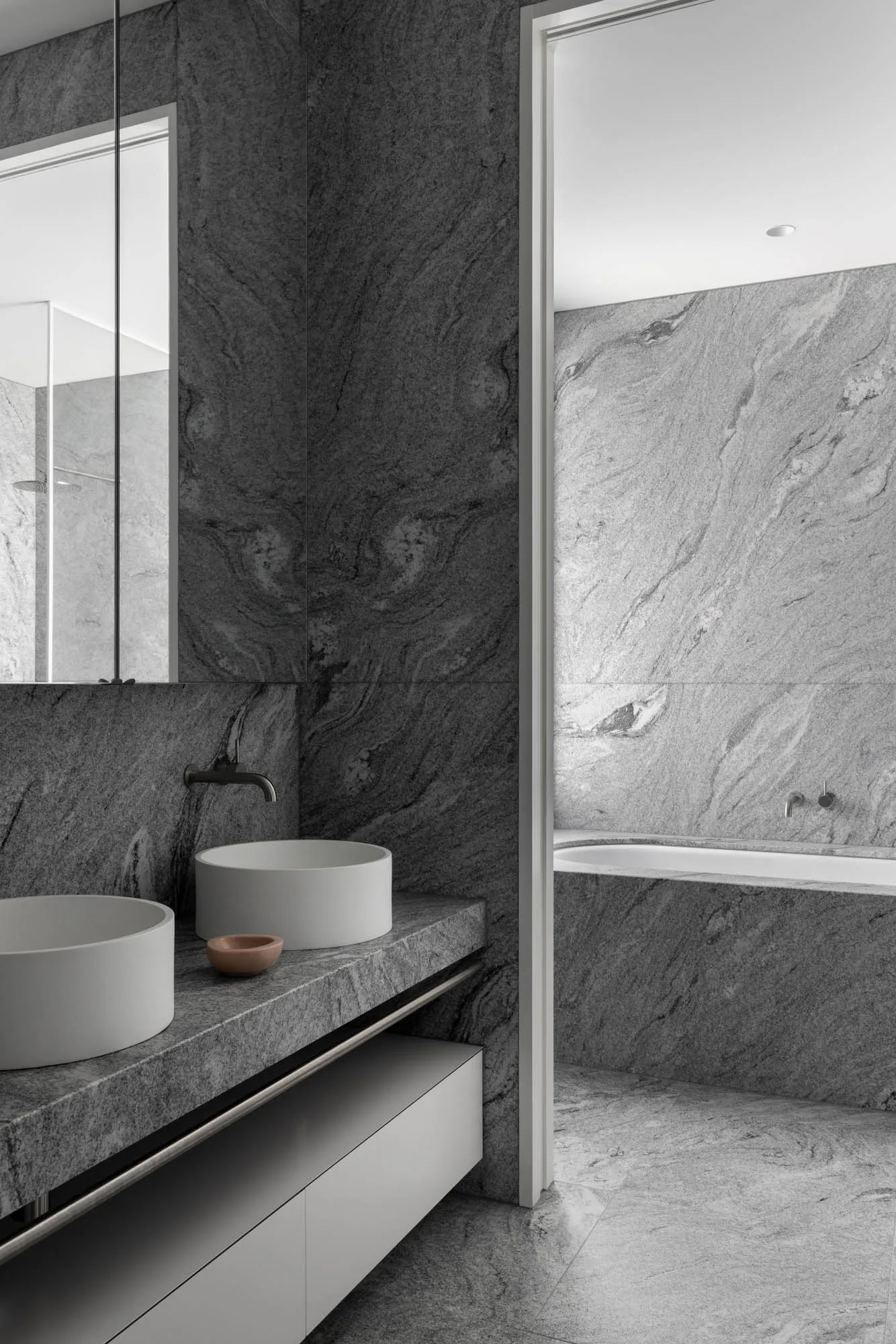 A modern bathroom featuring granite walls and marble sinks.