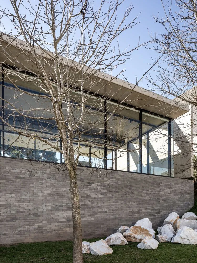 A modern house with a concrete exterior, large glass windows, and rocks in the foreground.