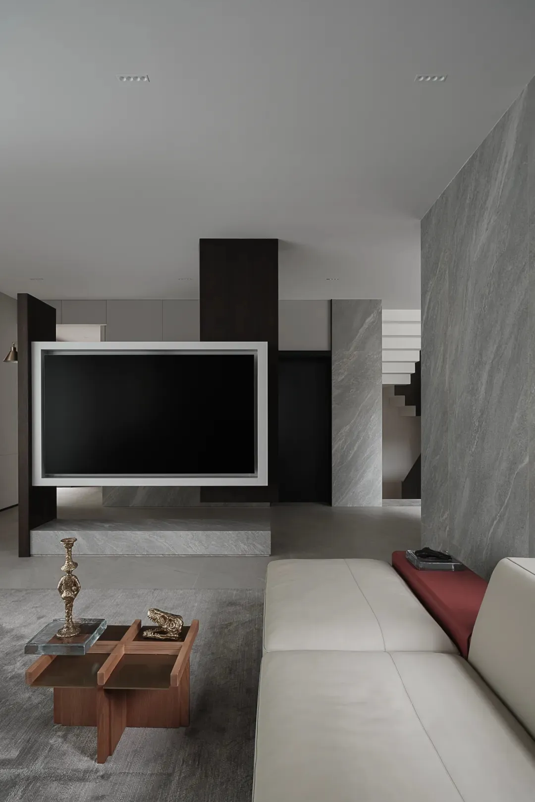 A modern living room with a white leather sofa, a marble coffee table, and a large television screen mounted on a marble colu